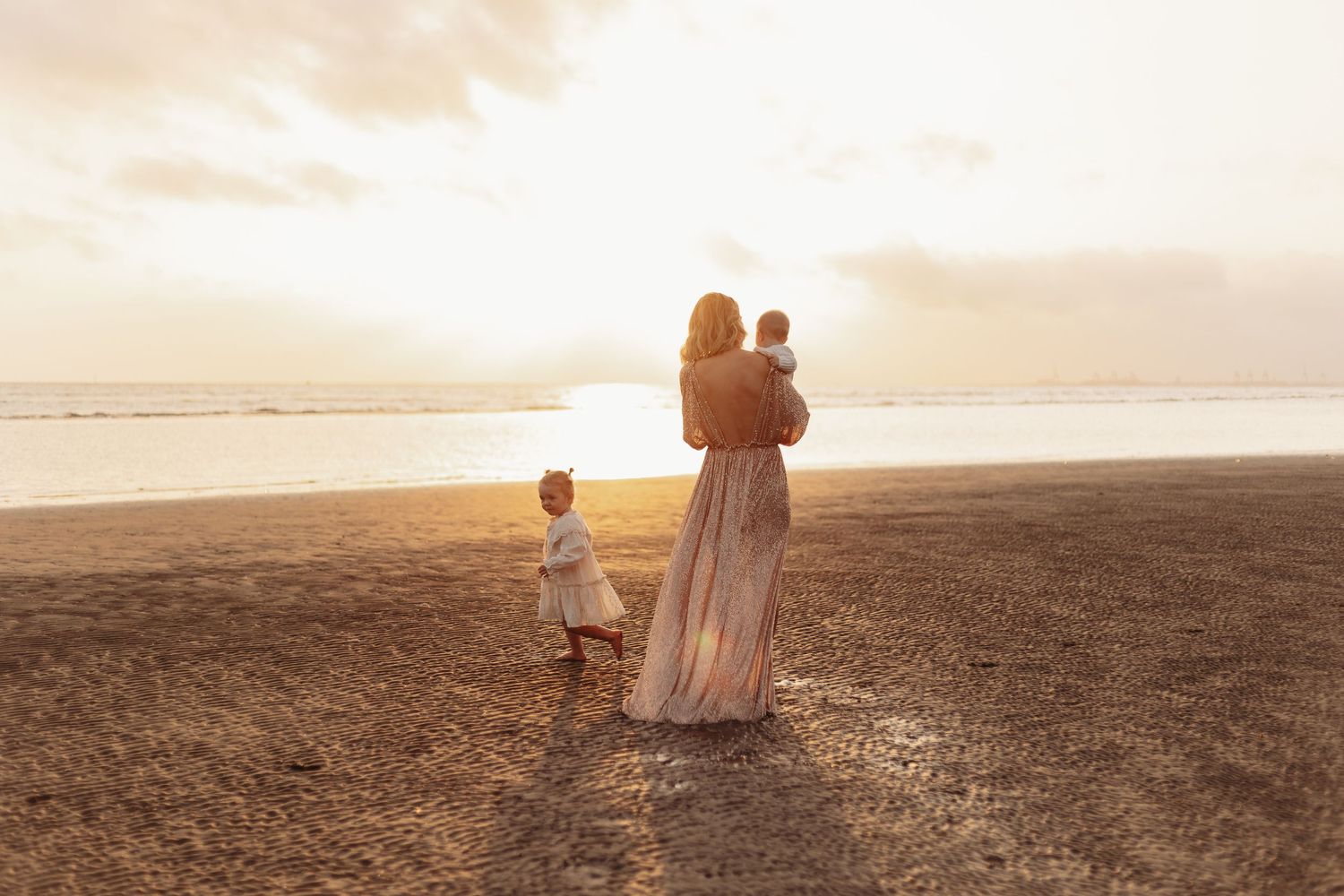 Silhouettes of three people standing on a beach at sunset, watching the golden sky over the ocean.