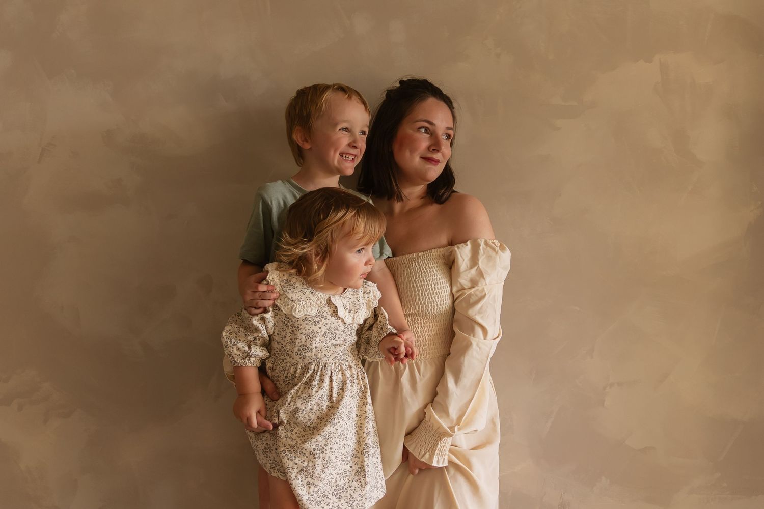 Joyful family portrait with cream-colored dresses against a neutral backdrop creating a warm, vintage aesthetic.