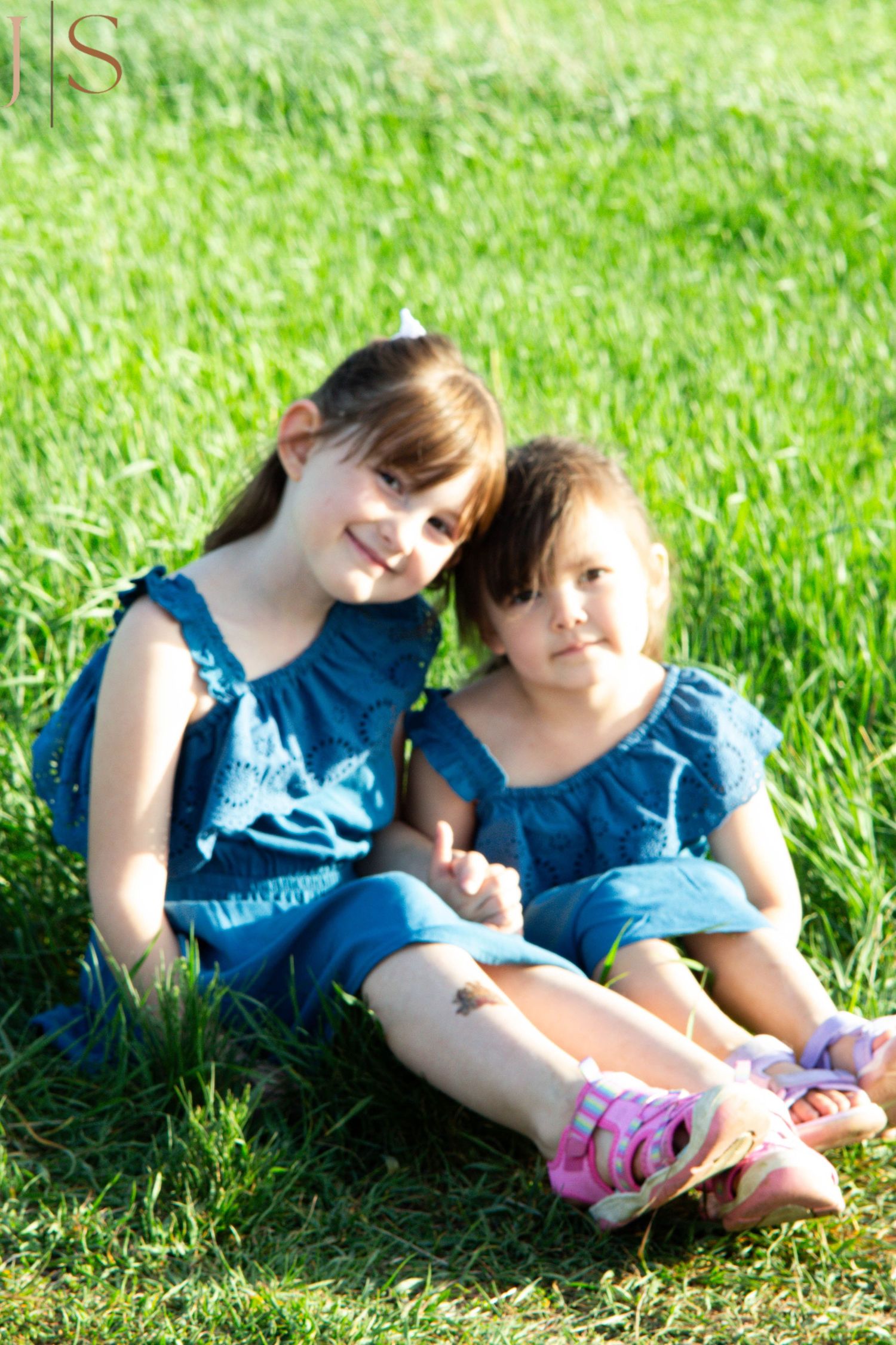 Two people in matching blue outfits lay together on bright green grass on a sunny day.