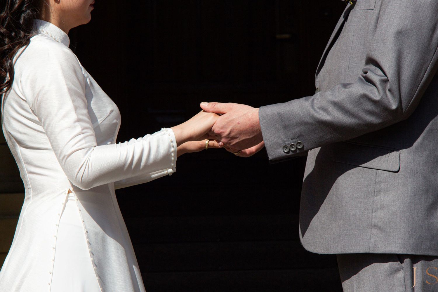Close up of hands during a wedding ceremony as a couple exchanges rings against a dark background.