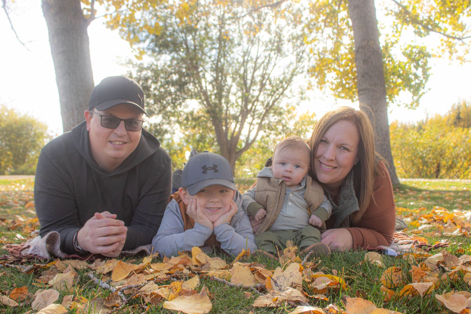 Family lying on fall leaves during autumn photoshoot in park.