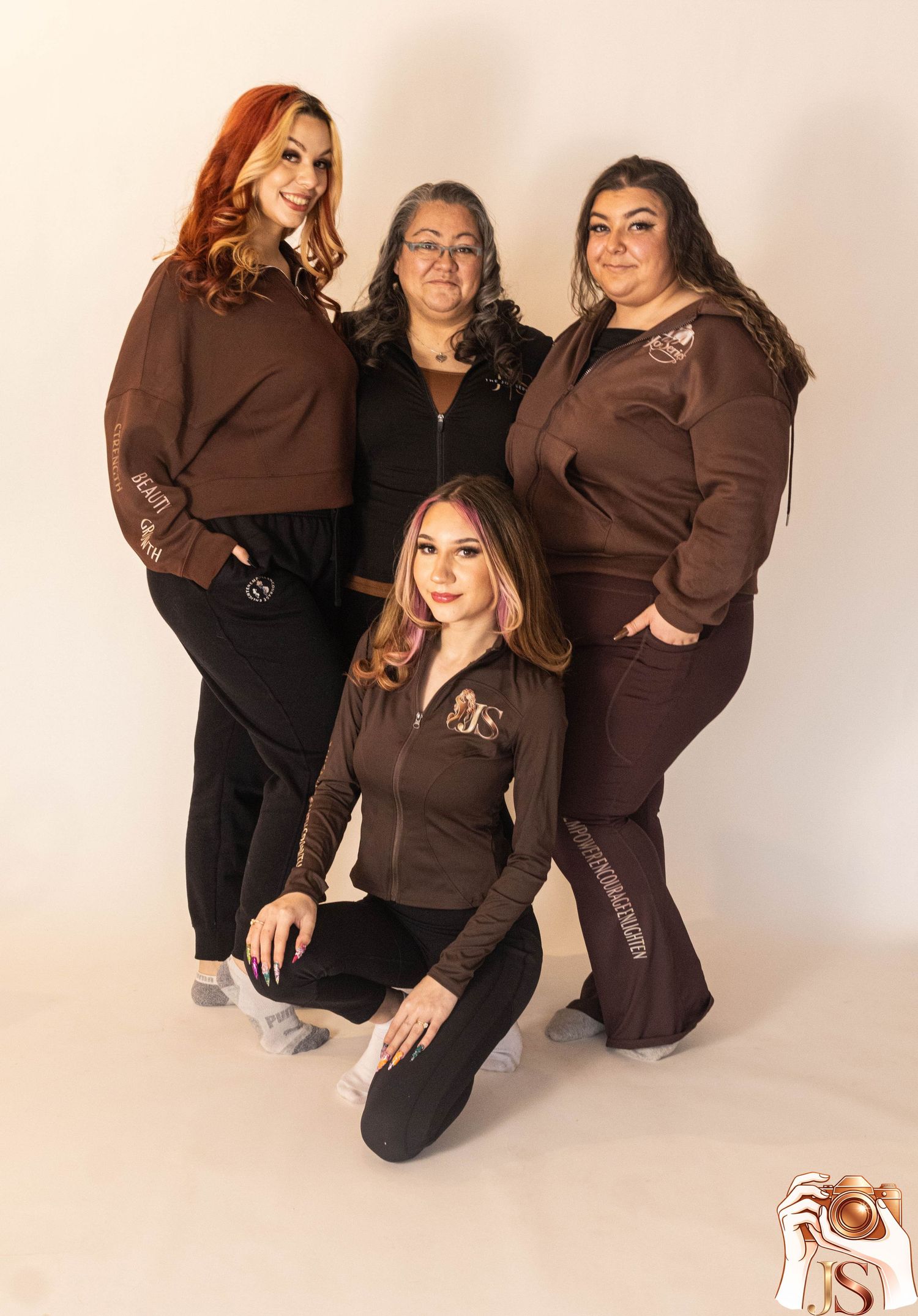 Group wearing matching brown and black outfits pose together in studio against white background.