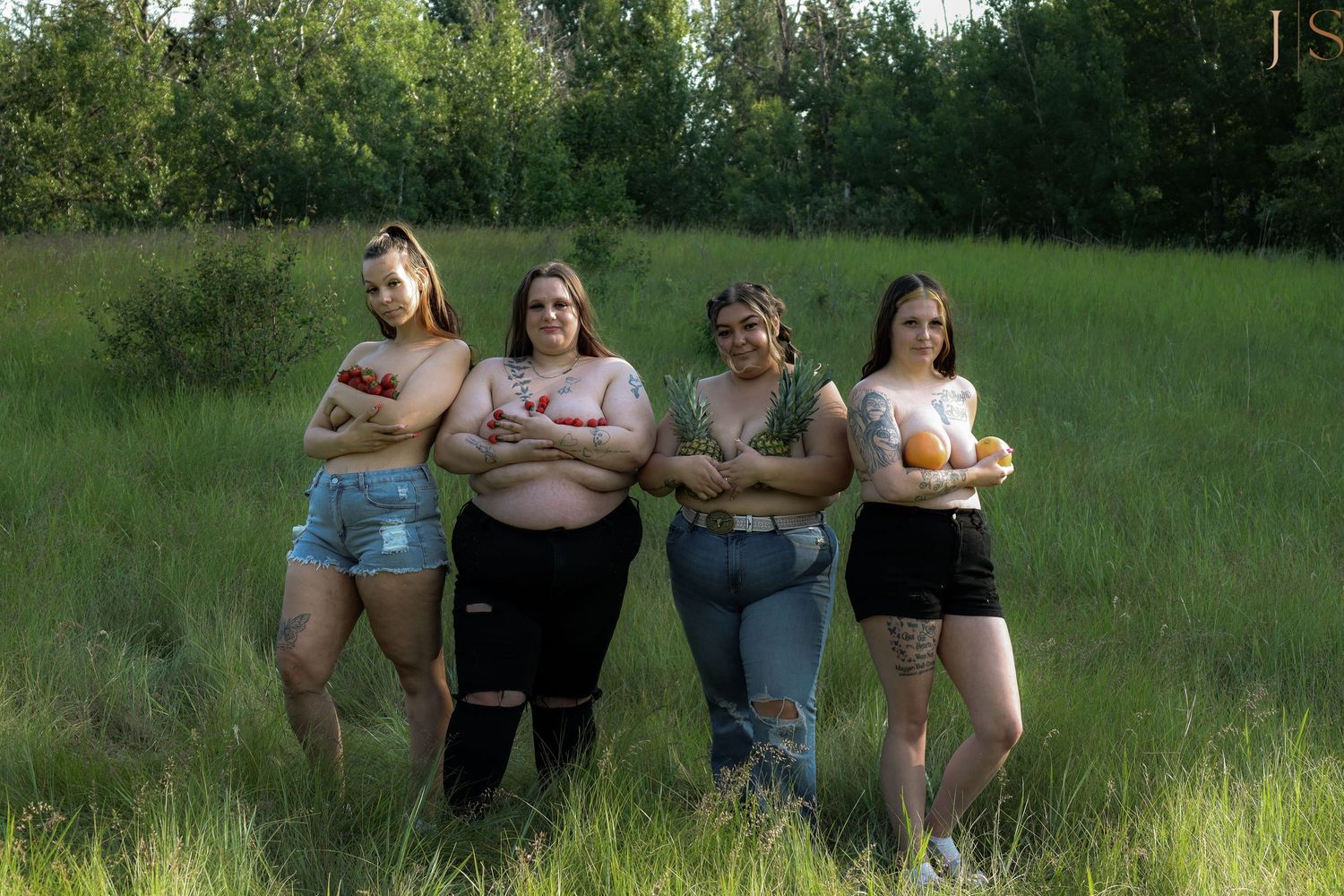 Four people pose together in a grassy field with green trees in the background on a sunny day.