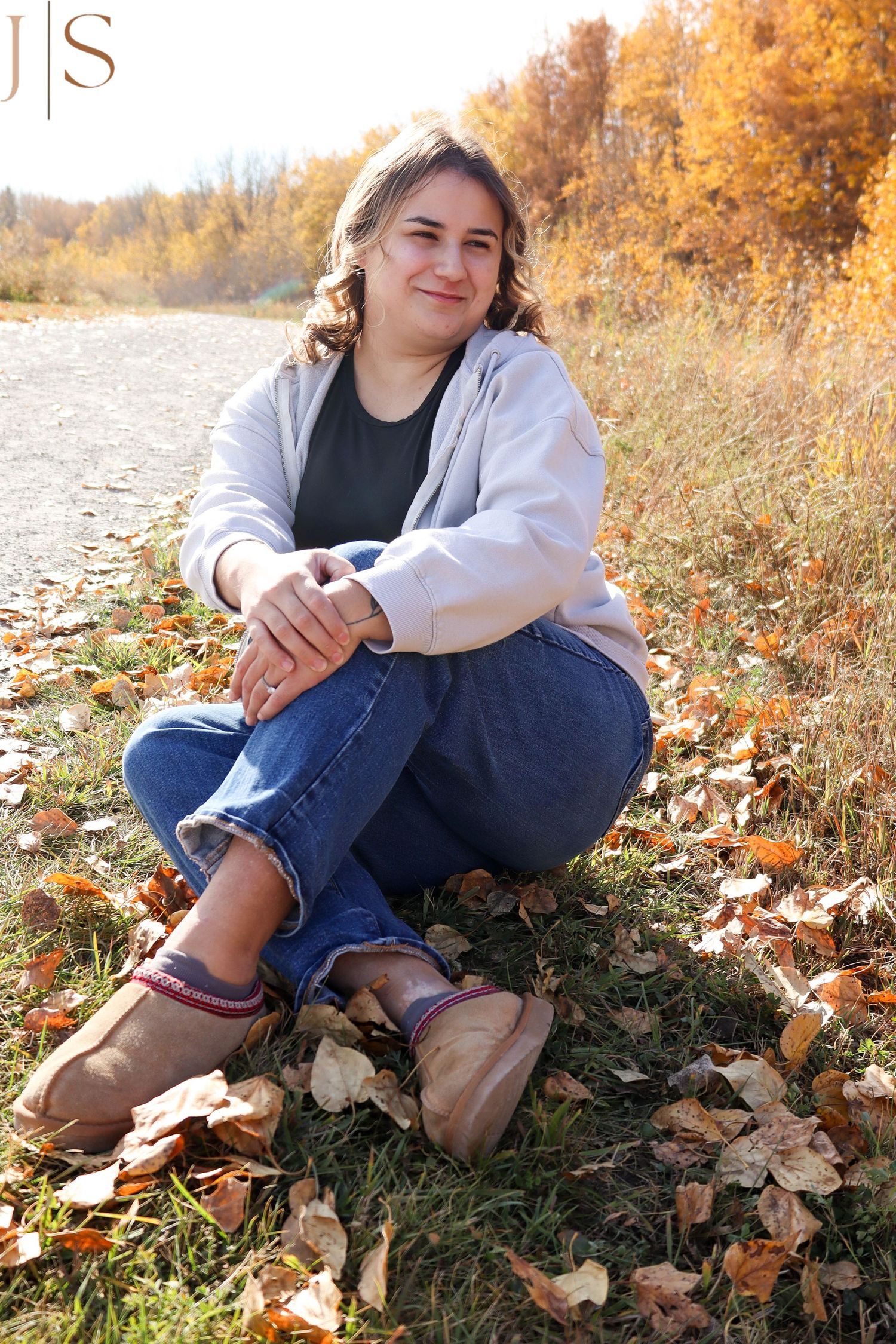 Person sitting in autumn leaves wearing jeans and boots against a backdrop of fall foliage.