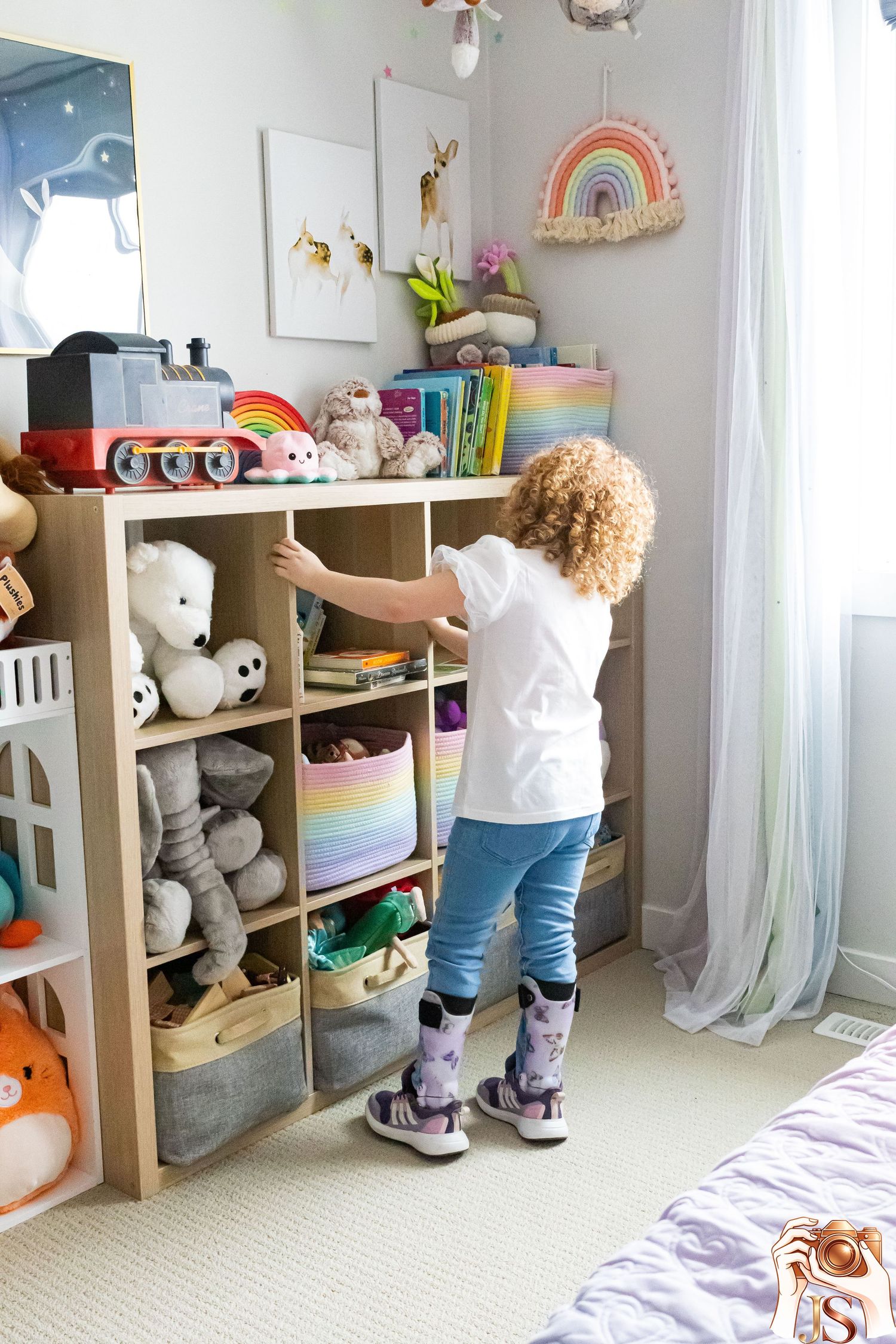 A child reaches for toys on wooden cube storage shelves filled with stuffed animals and plush toys in a bright playroom.