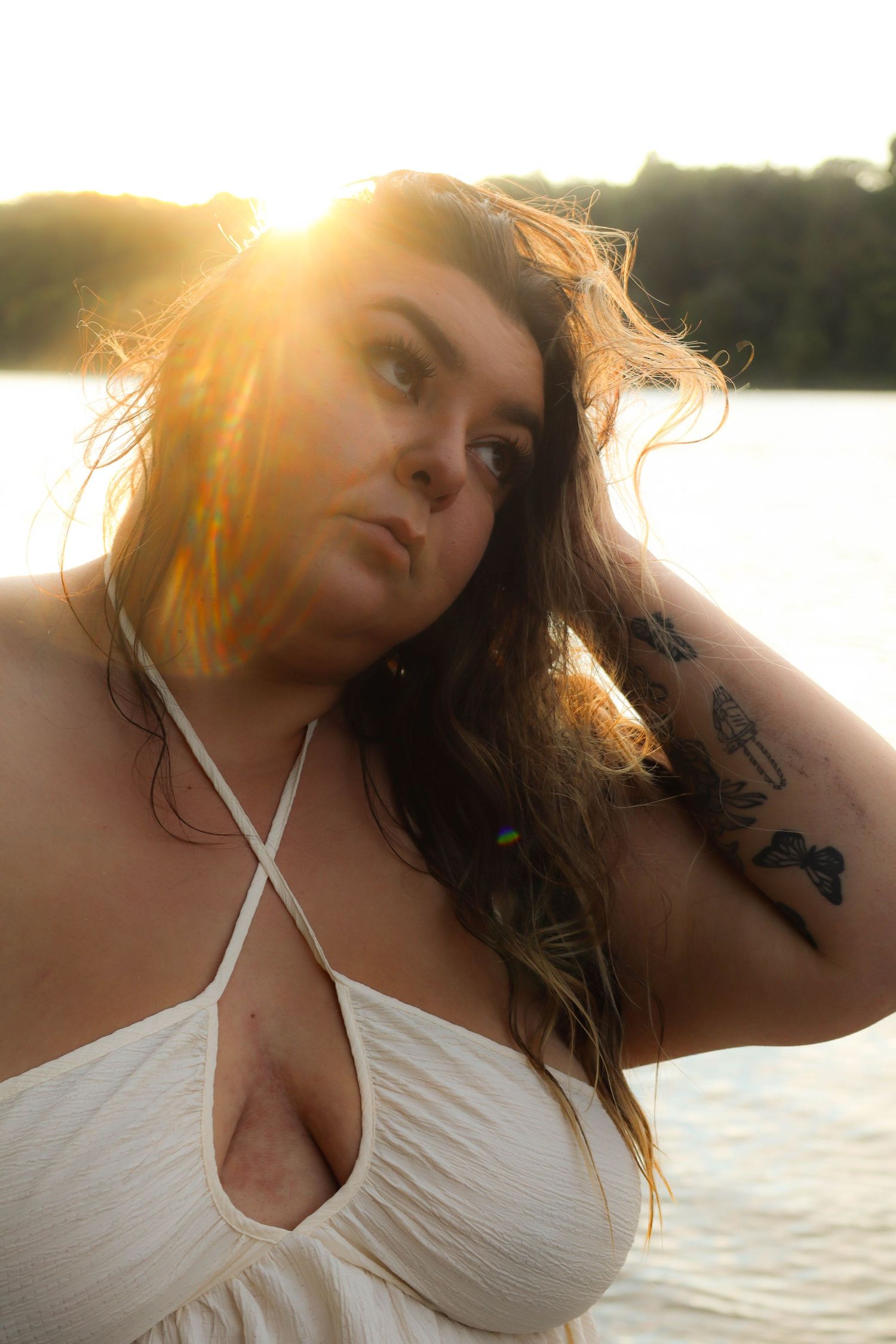 Portrait at sunset wearing a white halter top swimsuit with golden sunlight creating a warm backlit glow by the water.