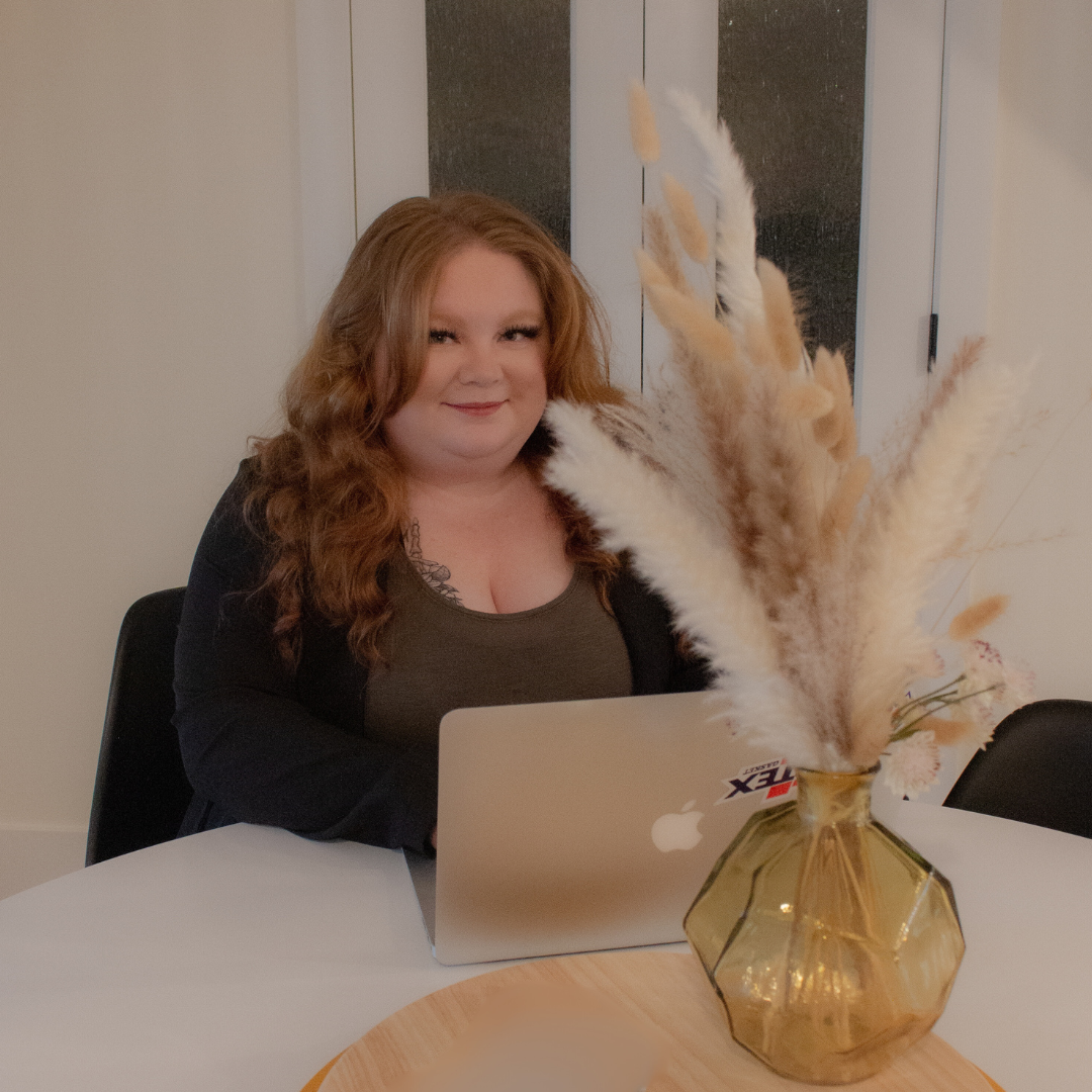 A workspace setup with a laptop, decorative pampas grass in amber vase, and comfortable office chair.
