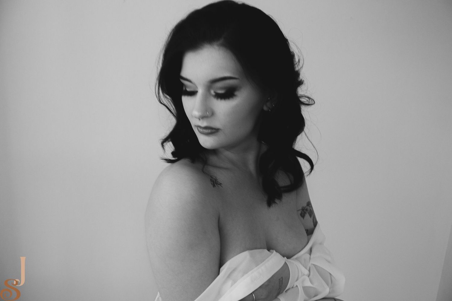 Black and white portrait of a person in an off-shoulder white garment looking down with dark wavy hair.