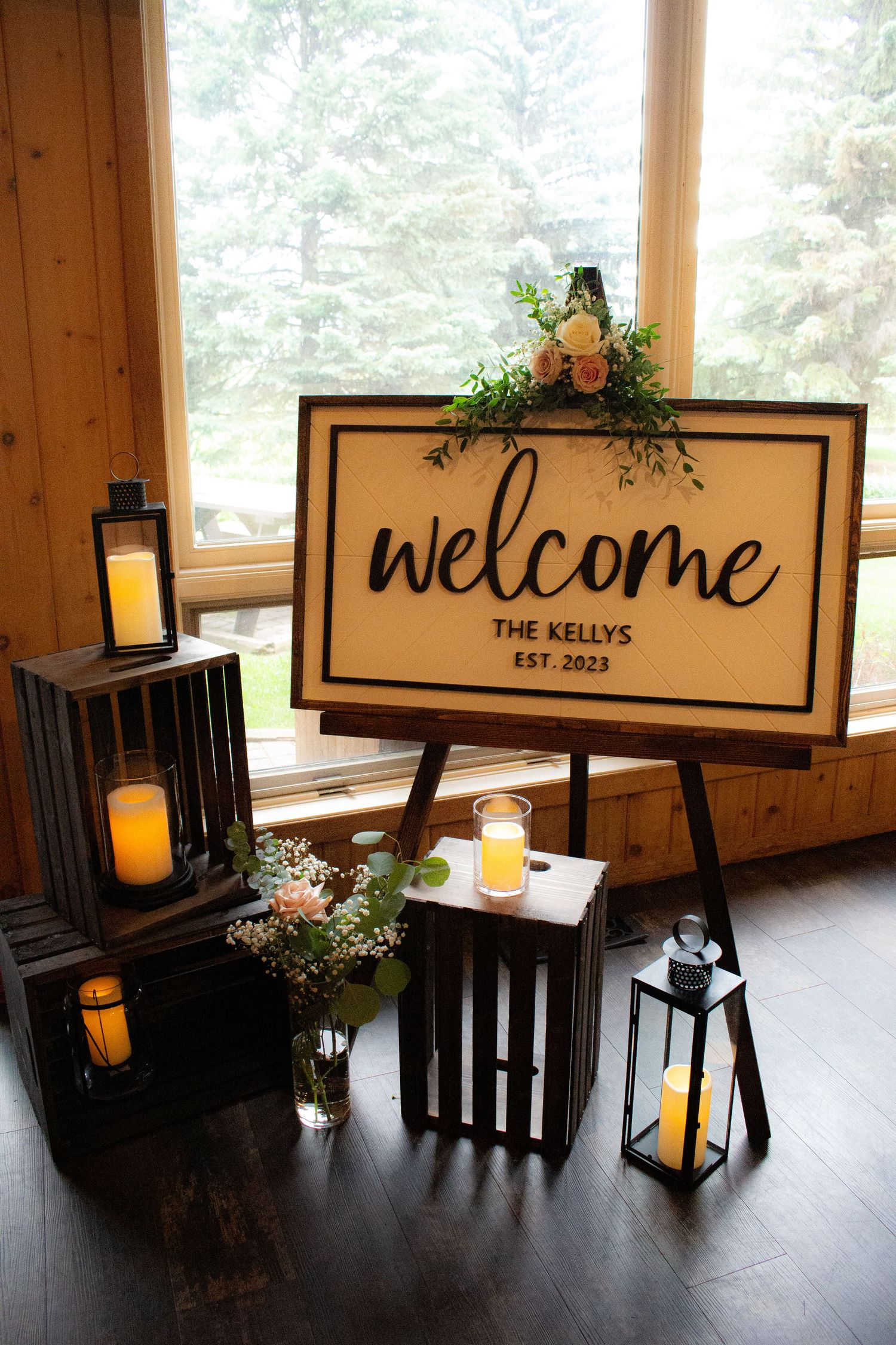 A rustic welcome sign display with lanterns and greenery in a wooden interior setting.