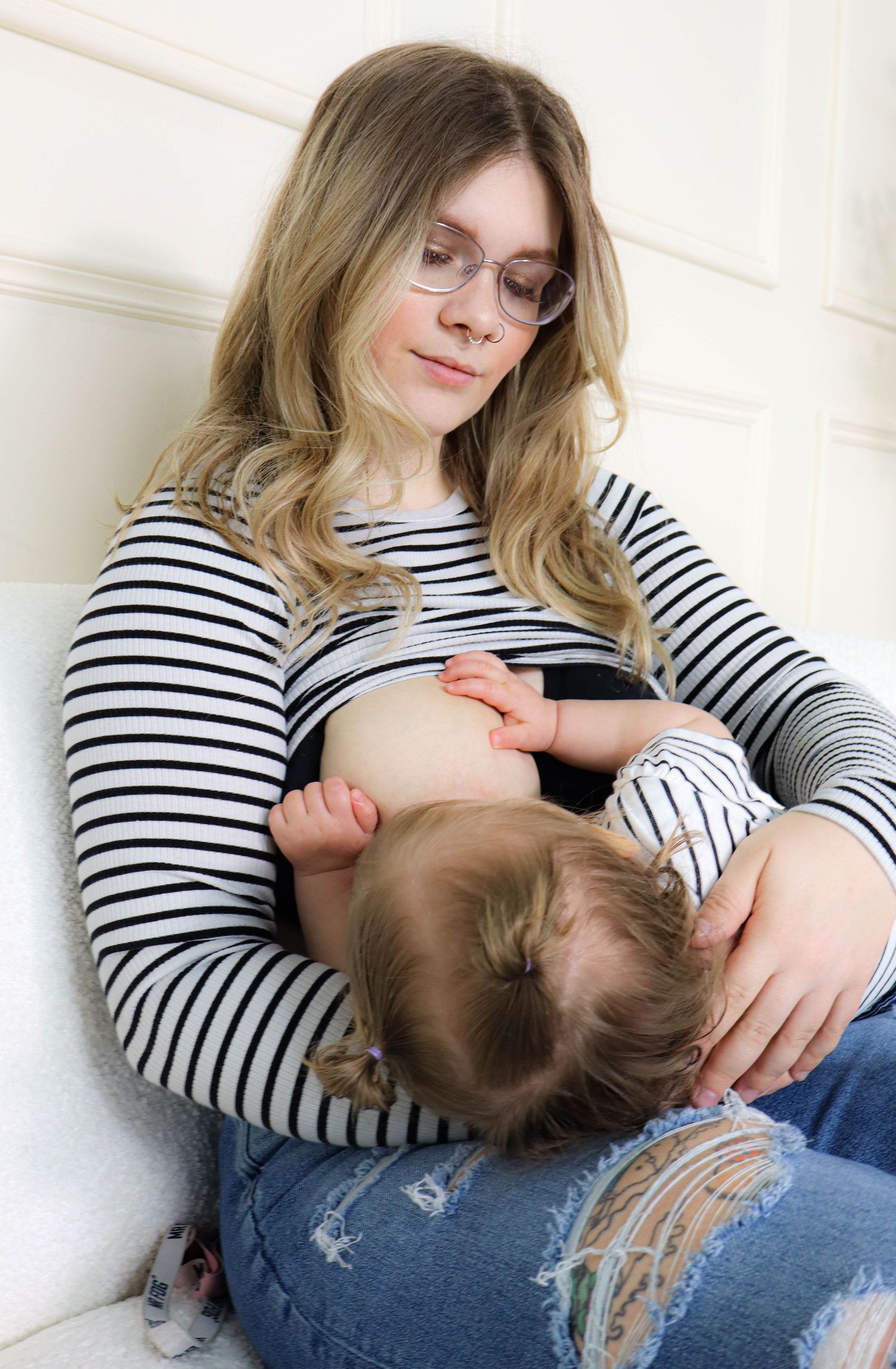 Tender moment between parent and child in striped shirt sitting against white wall.