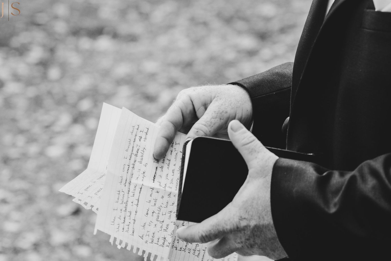 Black and white photograph showing hands holding a small notebook or document against a blurred background.