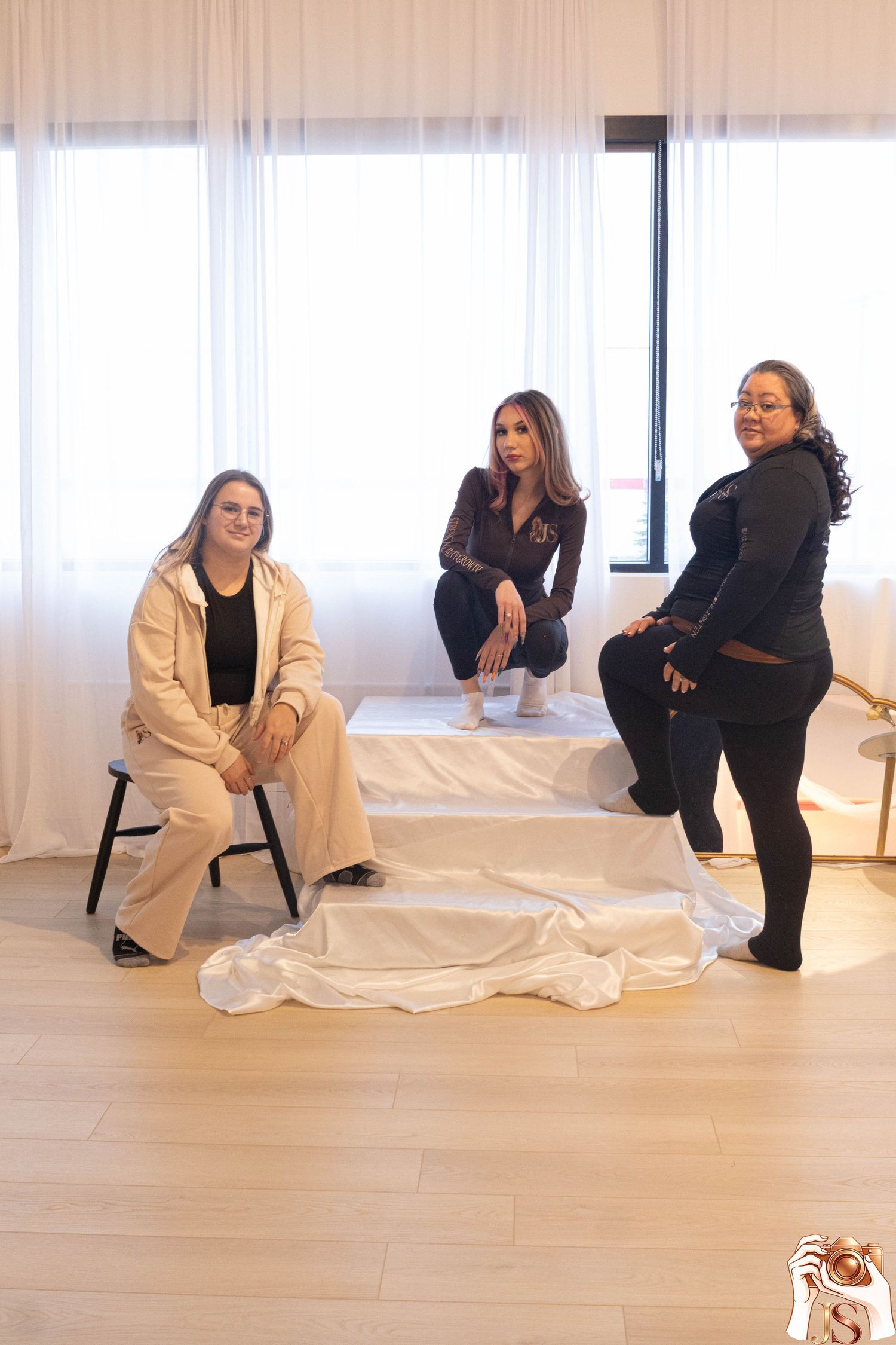 A group poses in a minimalist studio space wearing black and white outfits while sitting and standing on the floor.