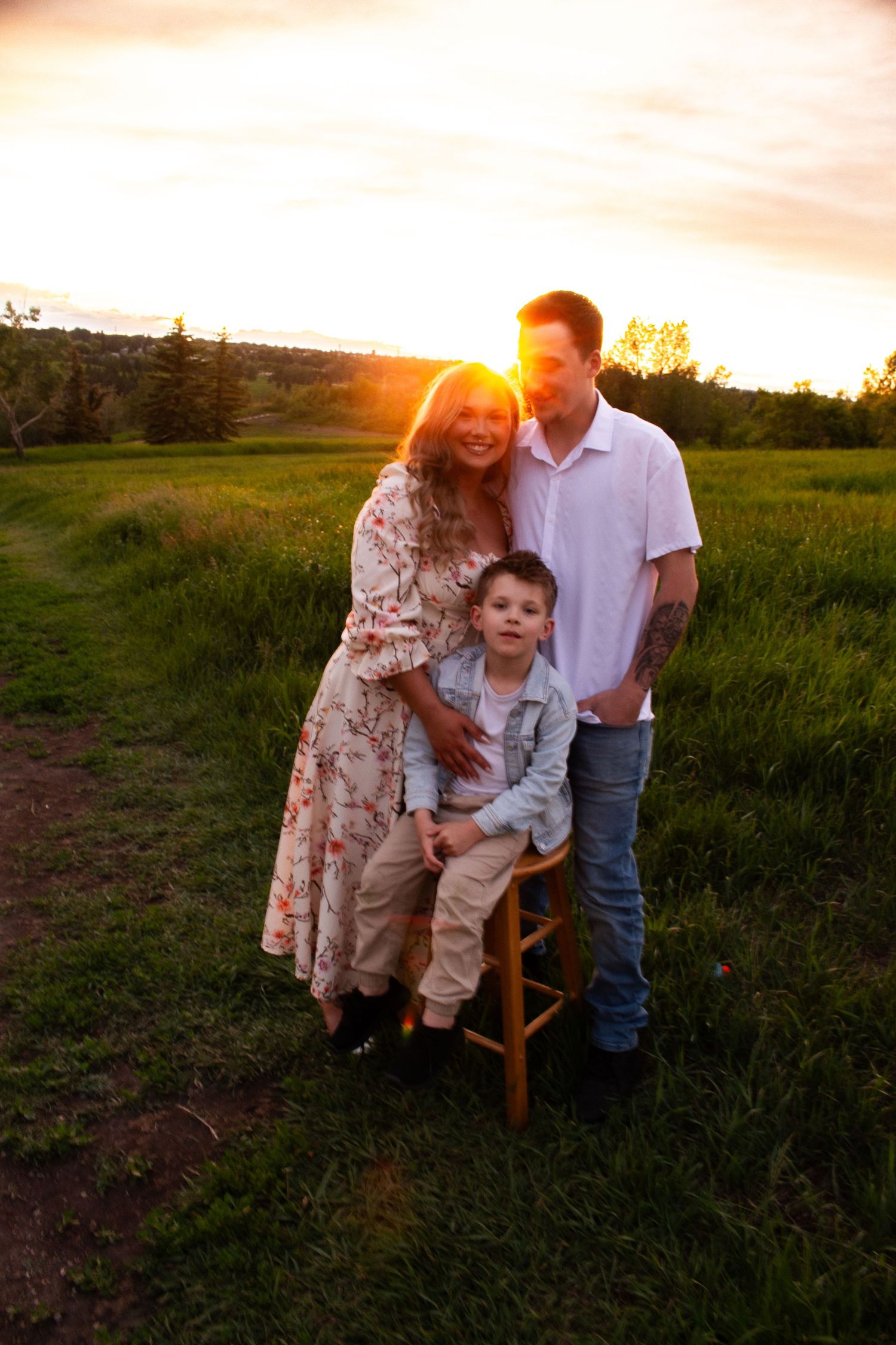 Sunset family portrait with wooden stool in grassy field.