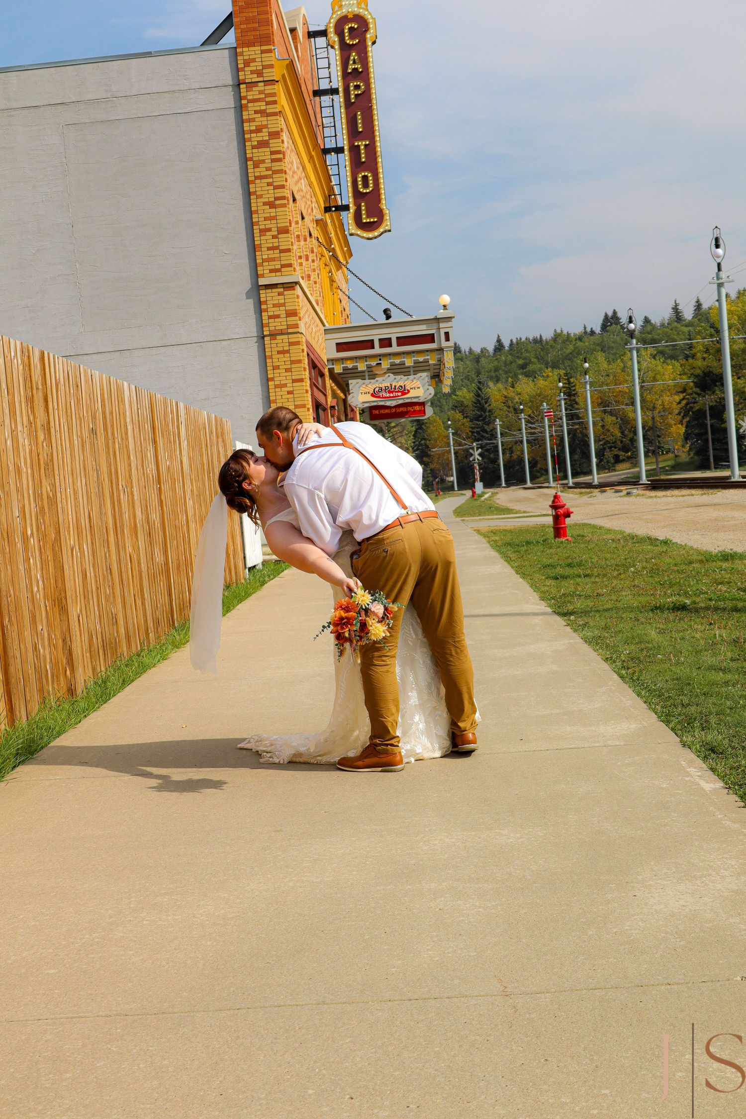 Couple takes creative wedding photos on a concrete path with a rustic building in the background.