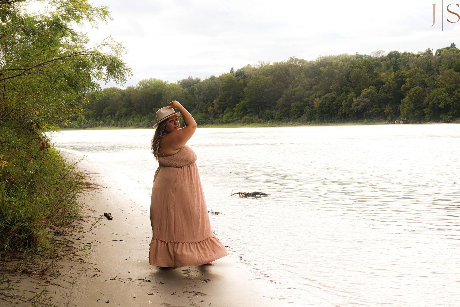 A person in a flowing pink dress stands at the edge of a serene lake during golden hour.