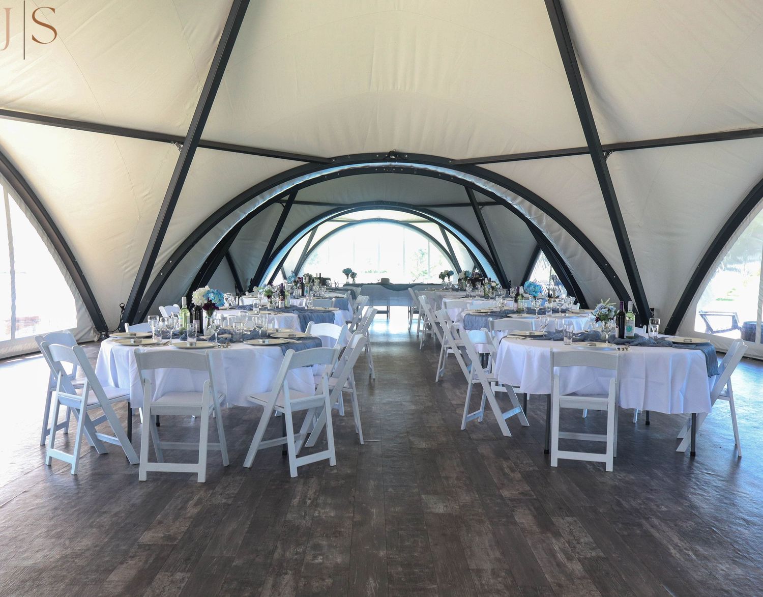 Wedding reception setup under a white dome tent with round tables and white folding chairs arranged for dining.