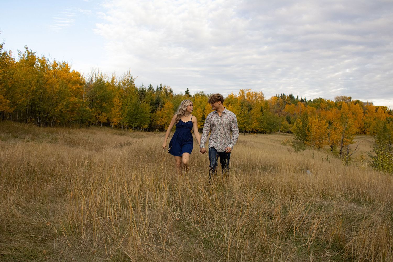 Couple walking together through golden autumn field at sunset.