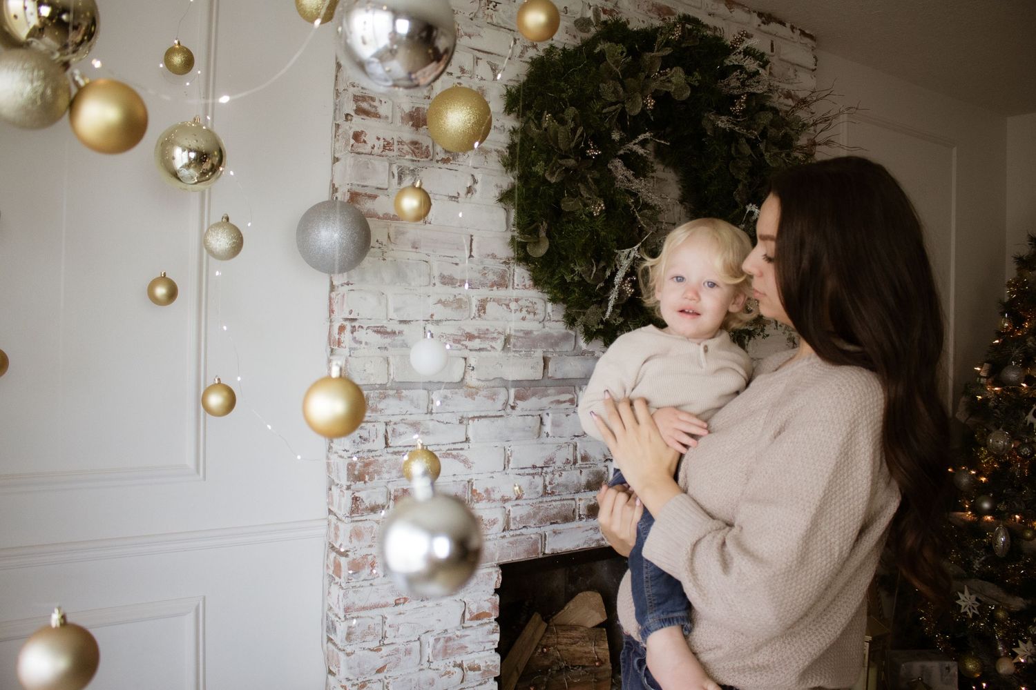 Festive holiday scene with mother and child surrounded by hanging gold ornaments.