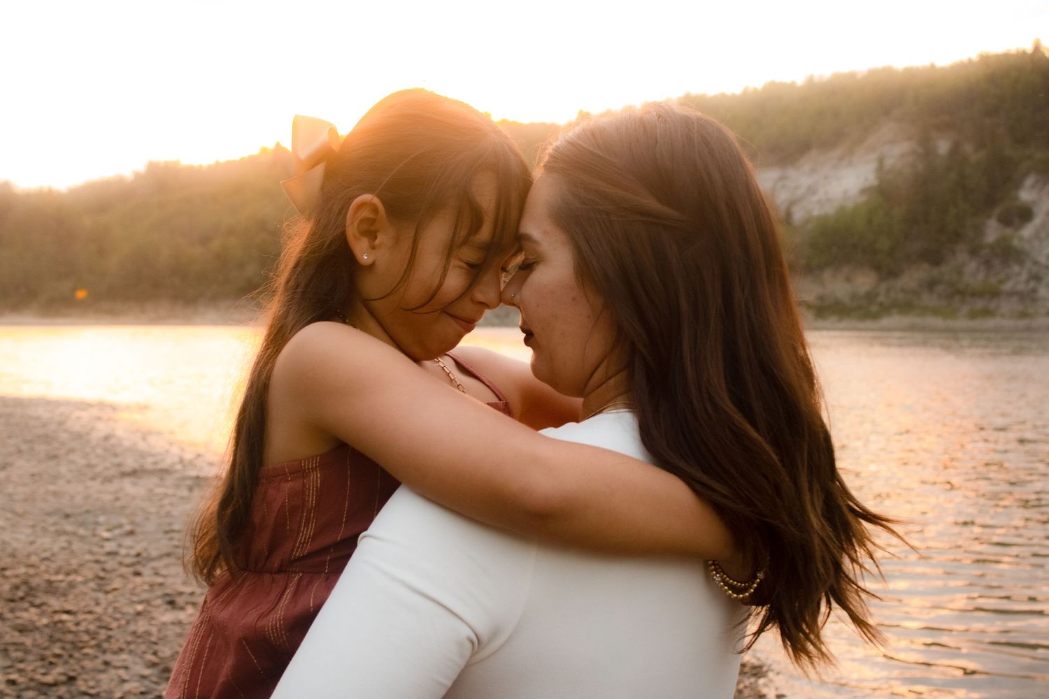 An intimate mother-child embrace captured during golden hour by the water.