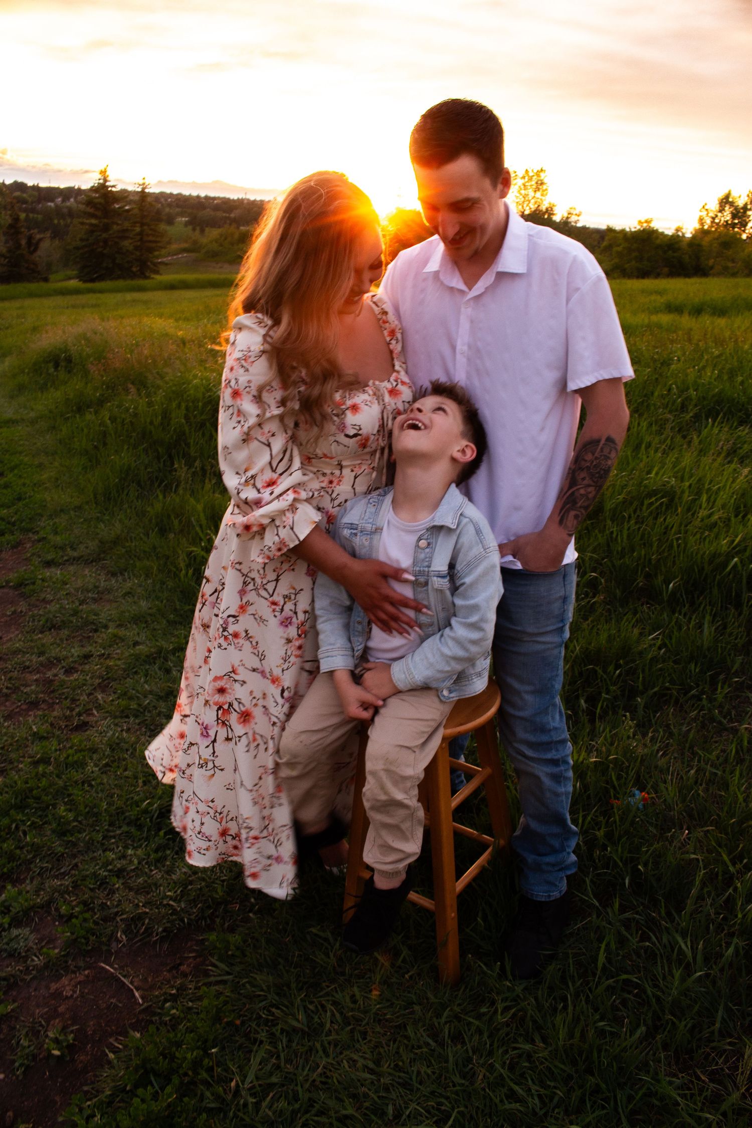 Family laughing together during golden hour photoshoot with wooden stool.
