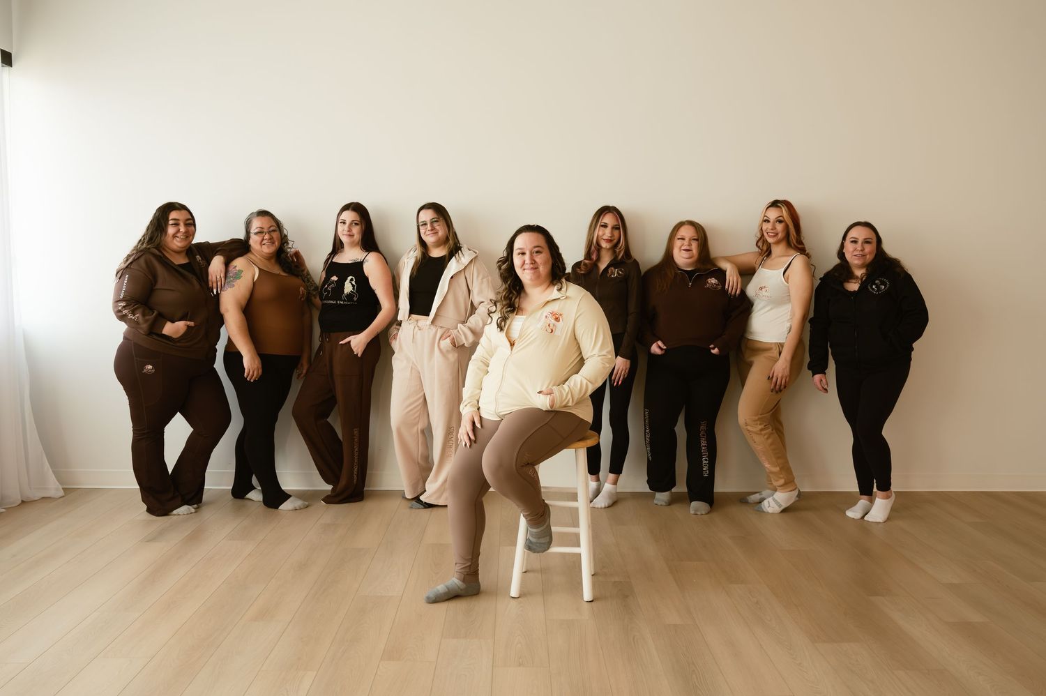 Group of ten women posing together in neutral tones in a bright studio setting.