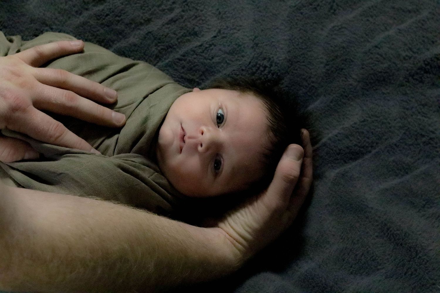 Intimate portrait of a young child resting on dark fabric.