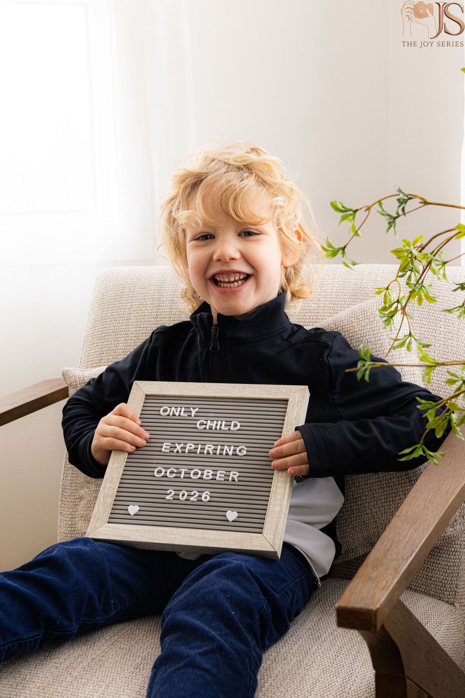 Smiling child holding a letterboard sign reading Only Child Expiring October 2026, announcing a new sibling.