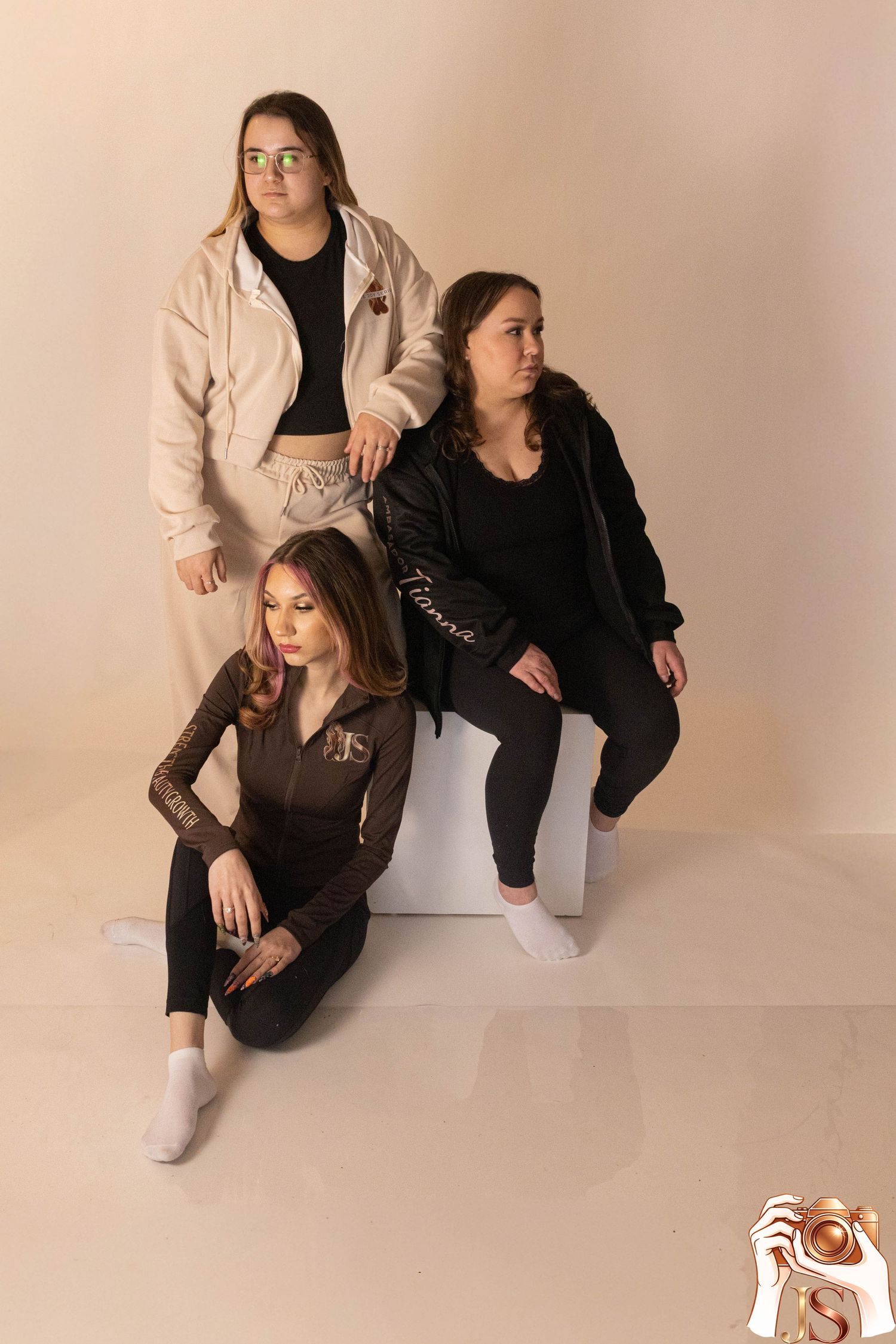 A group poses together in coordinated black and beige outfits against a neutral studio backdrop.