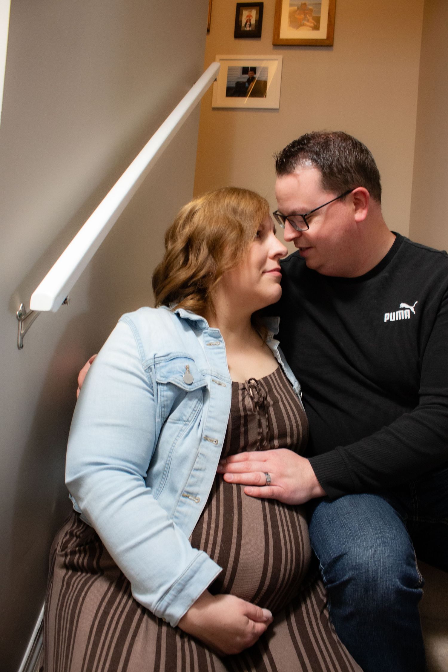 Intimate moment between couple on stairs during indoor maternity photoshoot.
