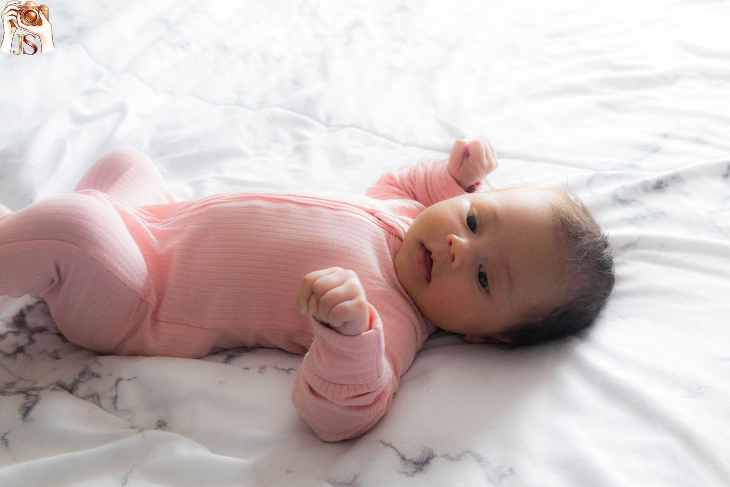 Baby in pink sleeper lying on white bedding stretches and moves in sequence of four photos.