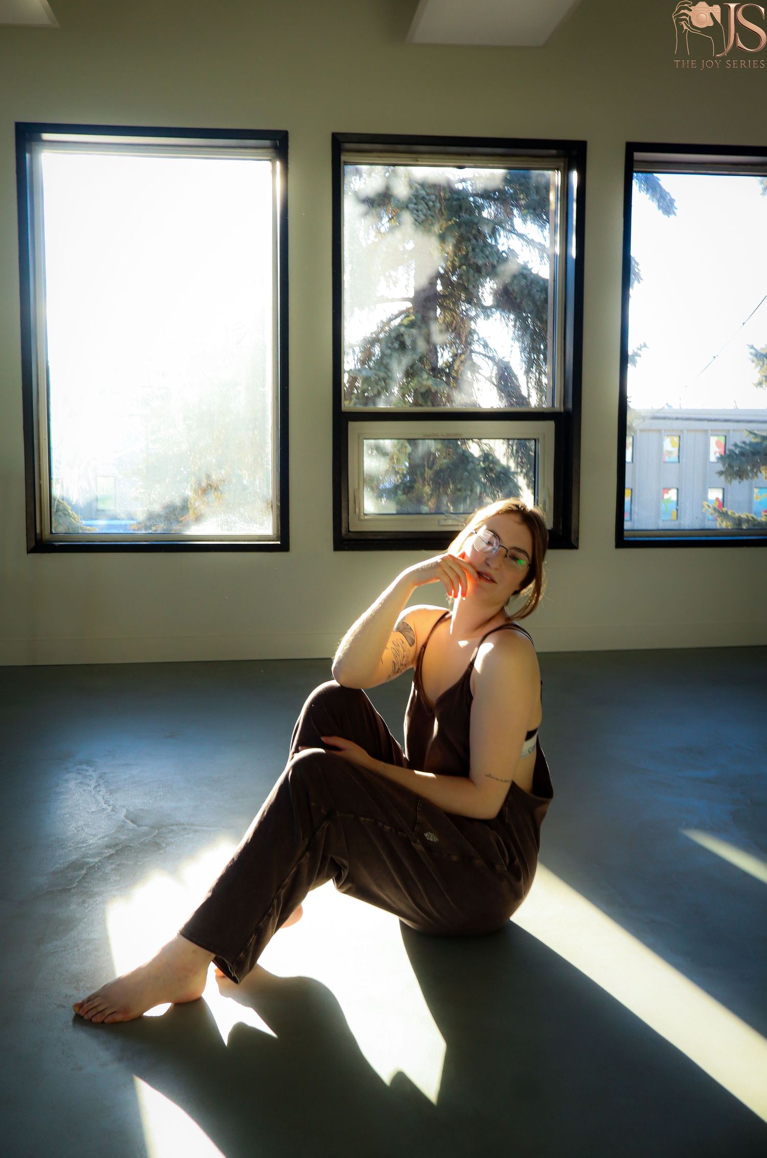 A person sits on a hardwood floor in sunlight streaming through large windows, creating dramatic shadows.