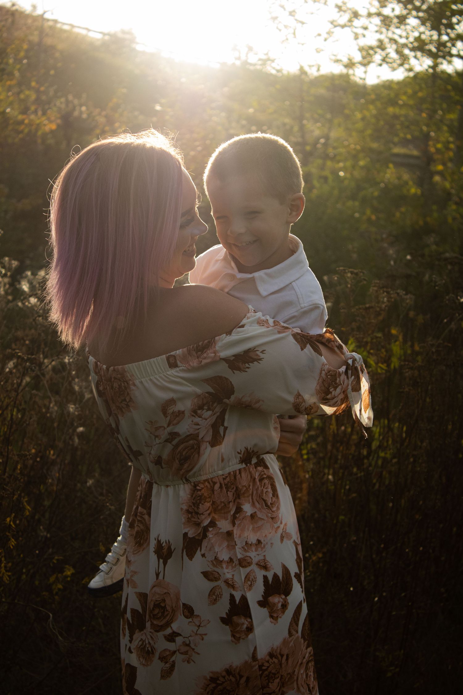 A tender moment in golden sunlight between a parent and child in a floral dress against a natural outdoor setting.