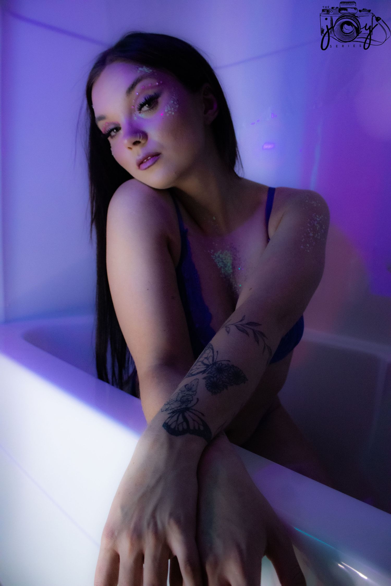 Artistic portrait in purple lighting showing tattoos on arm and creative mood lighting in bathroom setting.