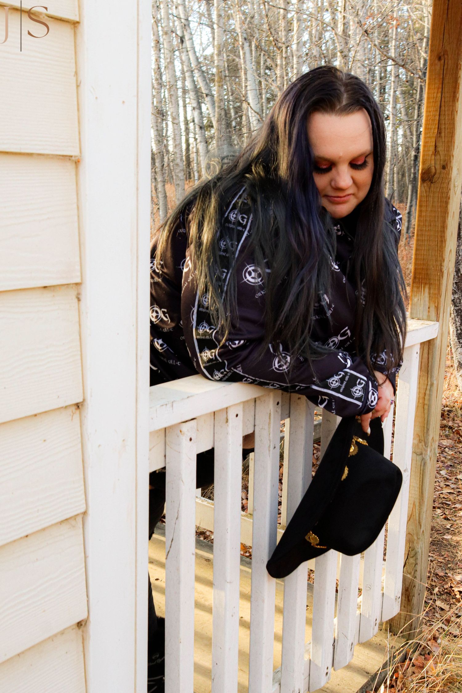 Figure leaning over white picket fence surrounded by winter trees.
