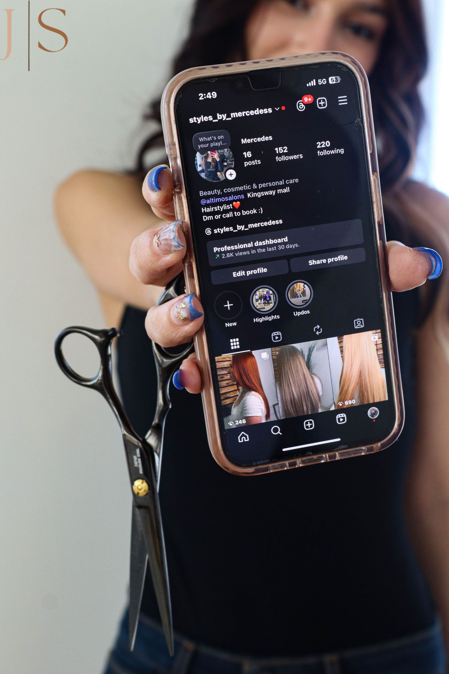 Someone with blue nail polish holds up an iPhone displaying a dark mode social media app interface with profile icons.
