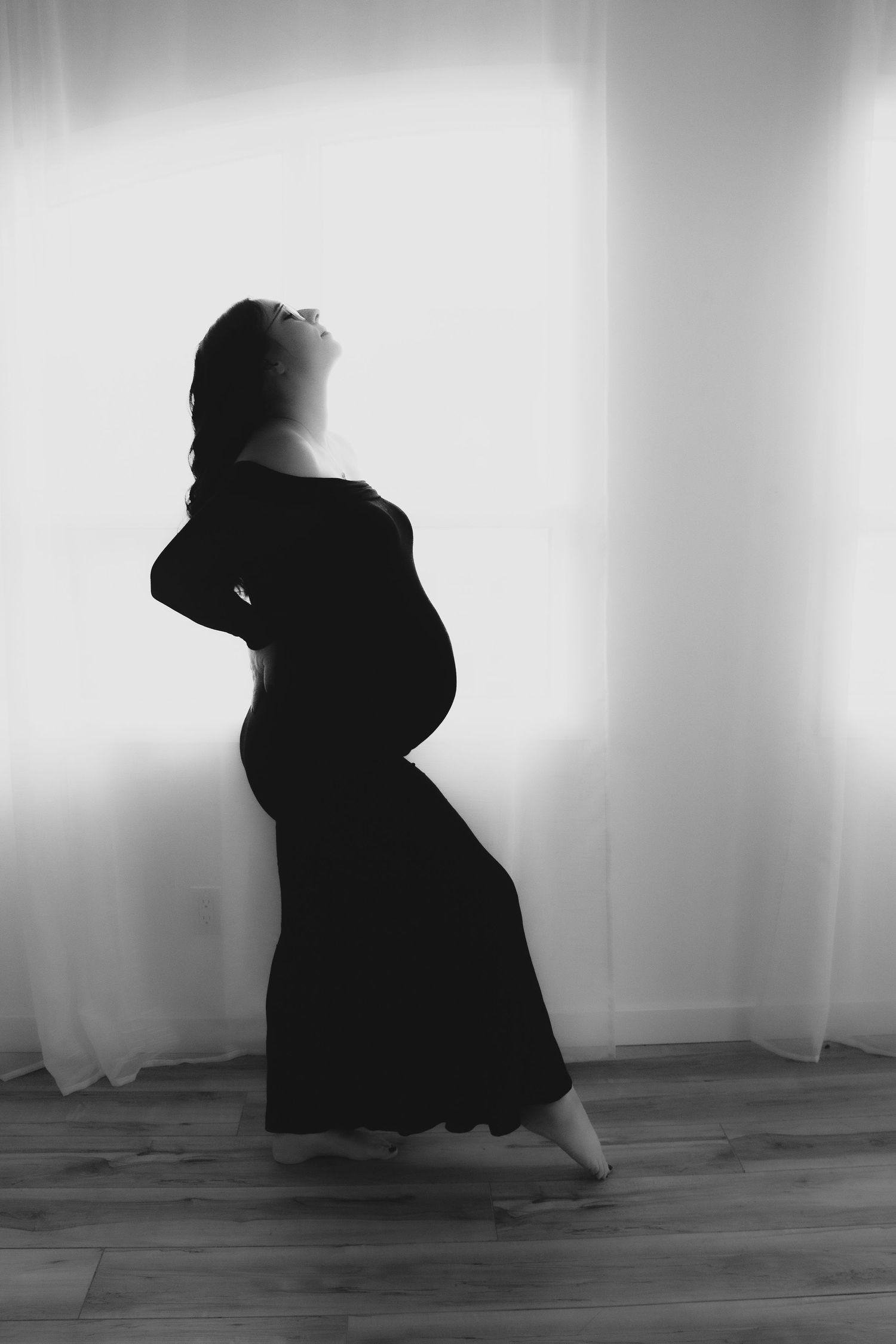 Artistic black and white silhouette of a pregnant woman in a flowing dress against a light background.