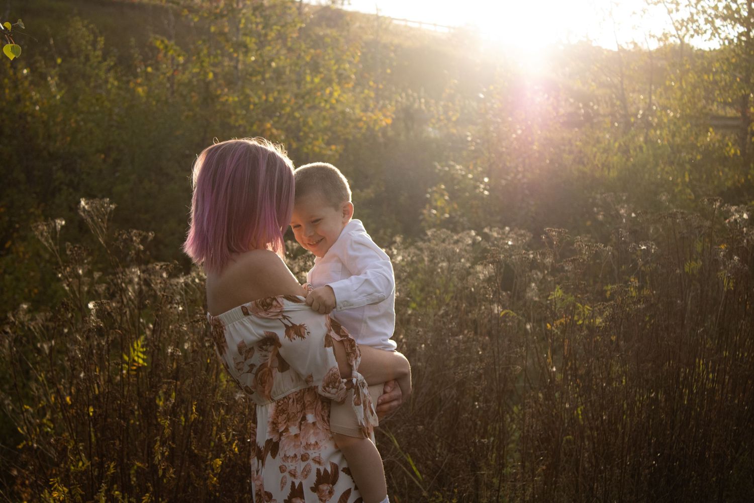 Parent holding child in floral dress during golden hour photoshoot.