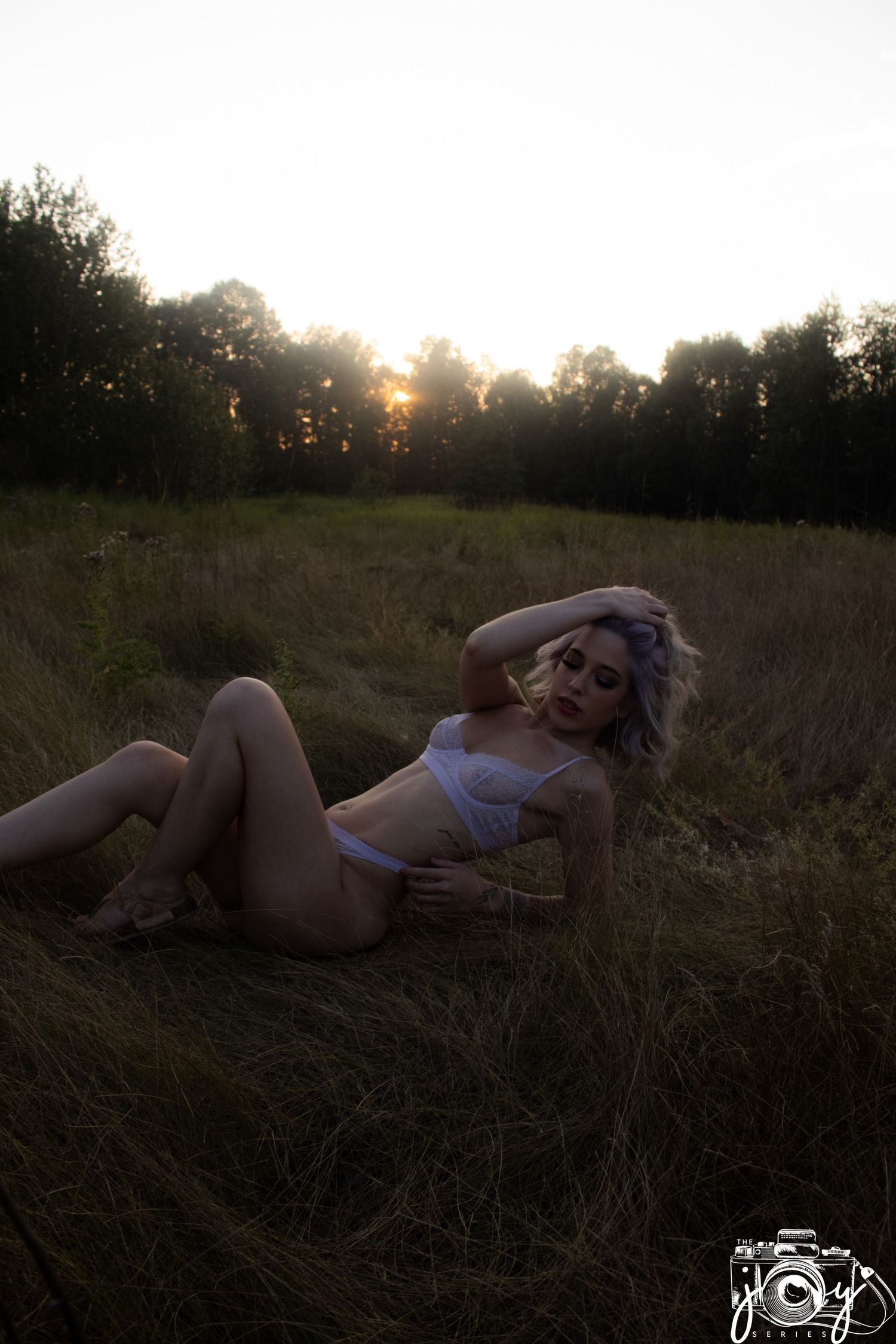 A silhouetted figure reclining in tall grass at sunset with trees in the background.