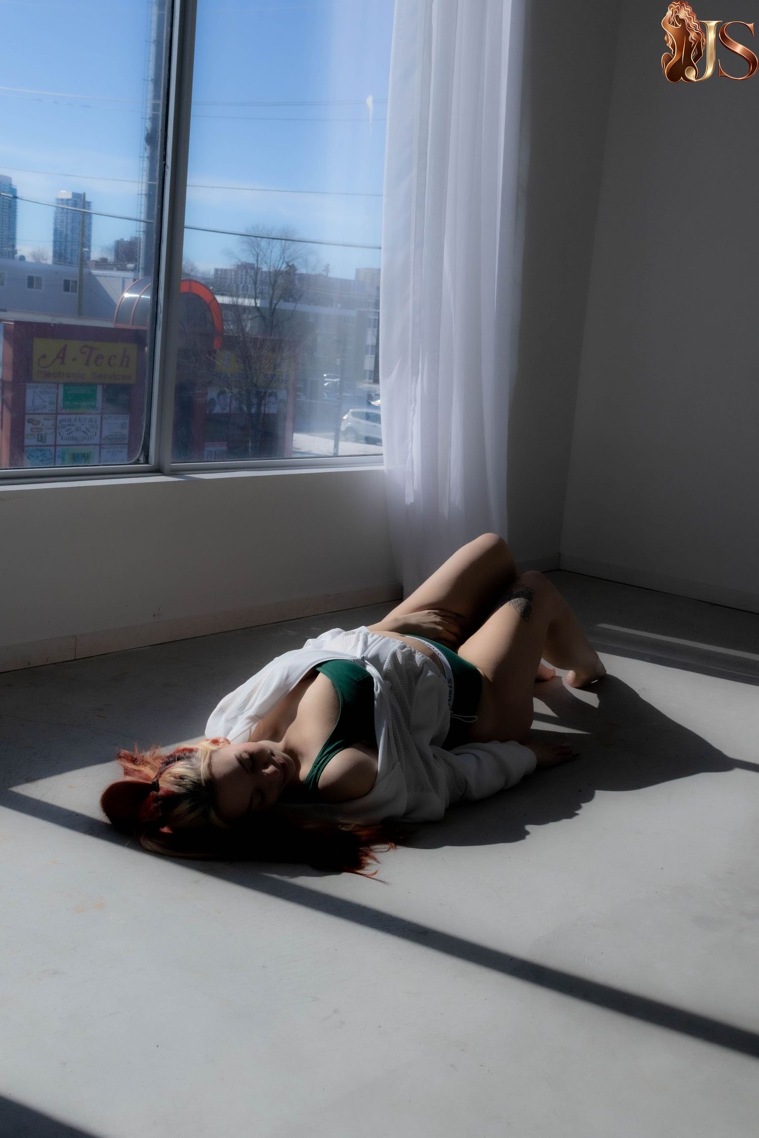 Person lying on floor in sunlit room with windows casting dramatic shadows.