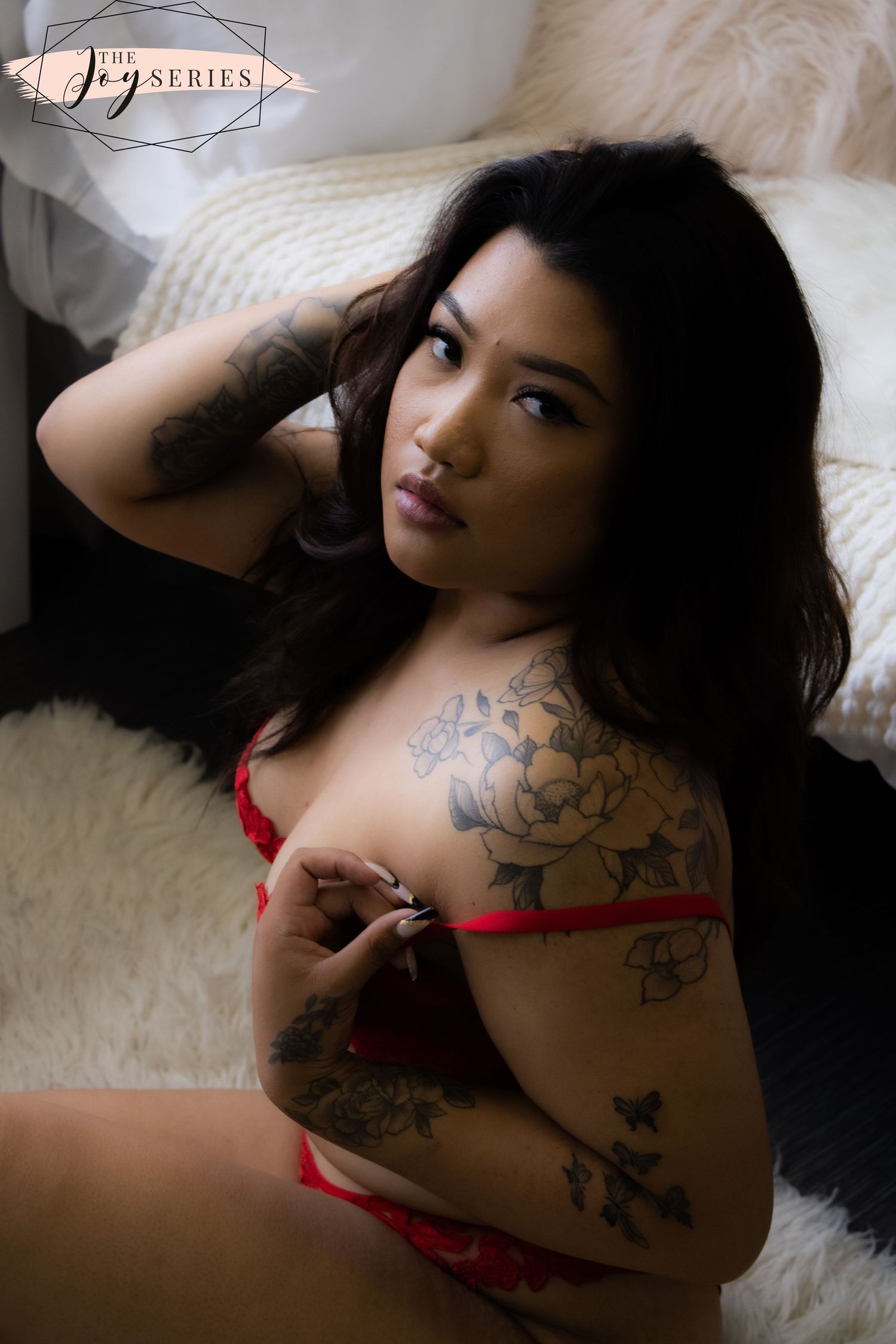 Figure in red lingerie poses on white bedding showing floral tattoo artwork.