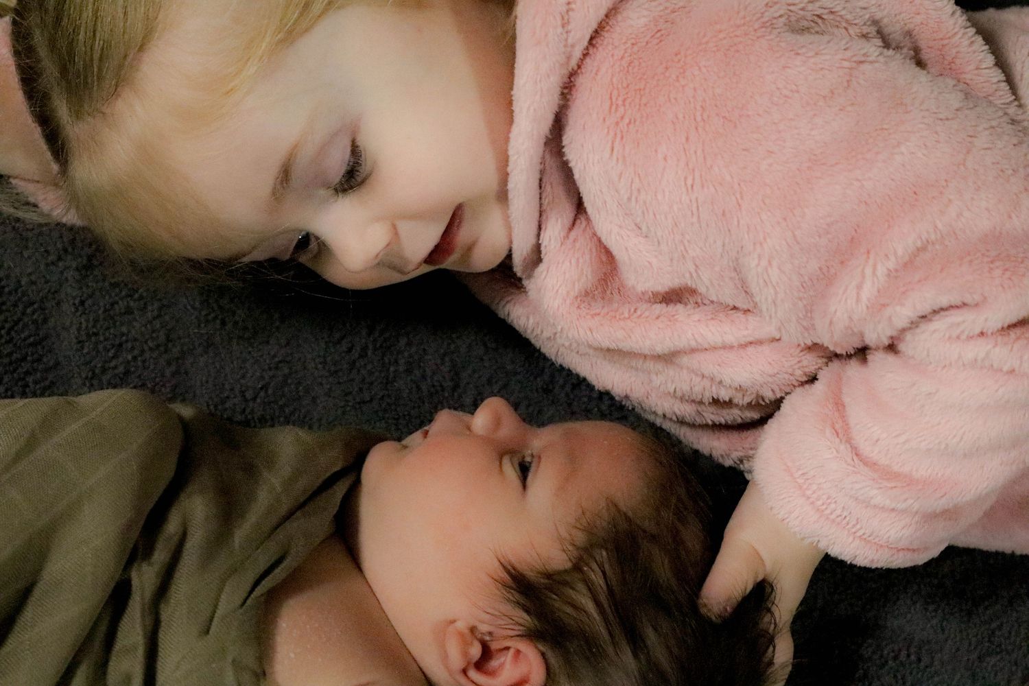 Two small children resting peacefully on dark bedding.
