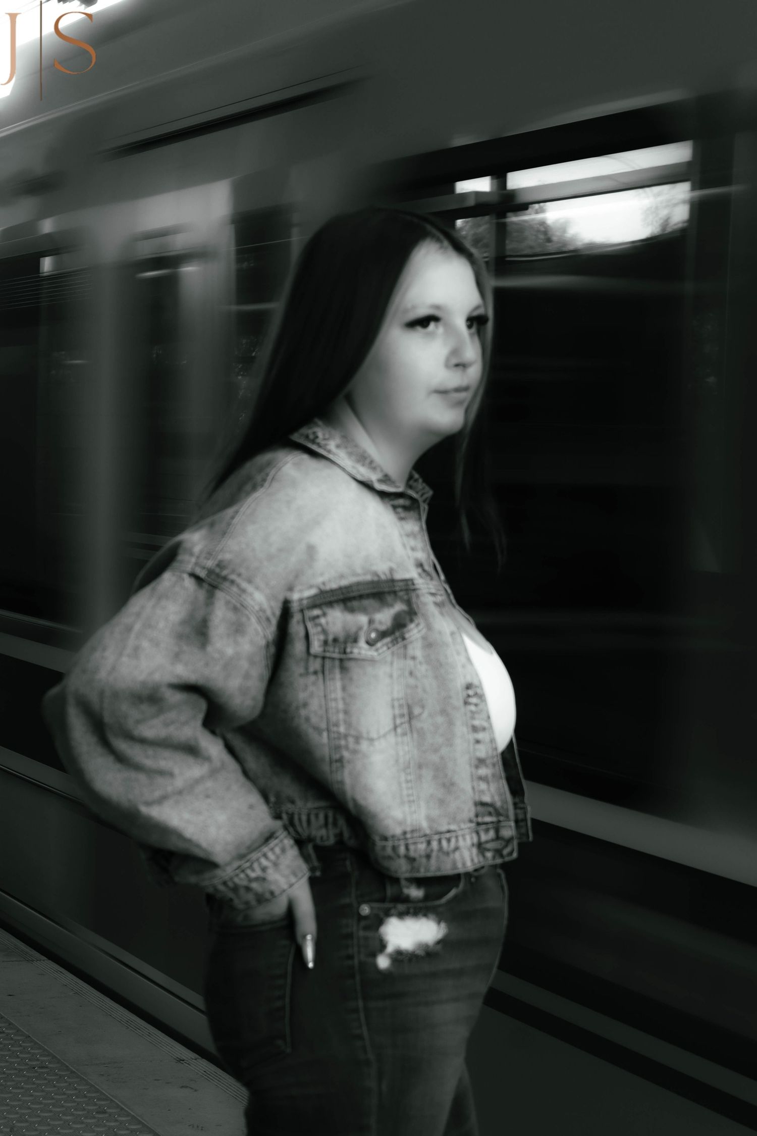 Blurred figure in denim stands on subway platform in moody black and white composition.