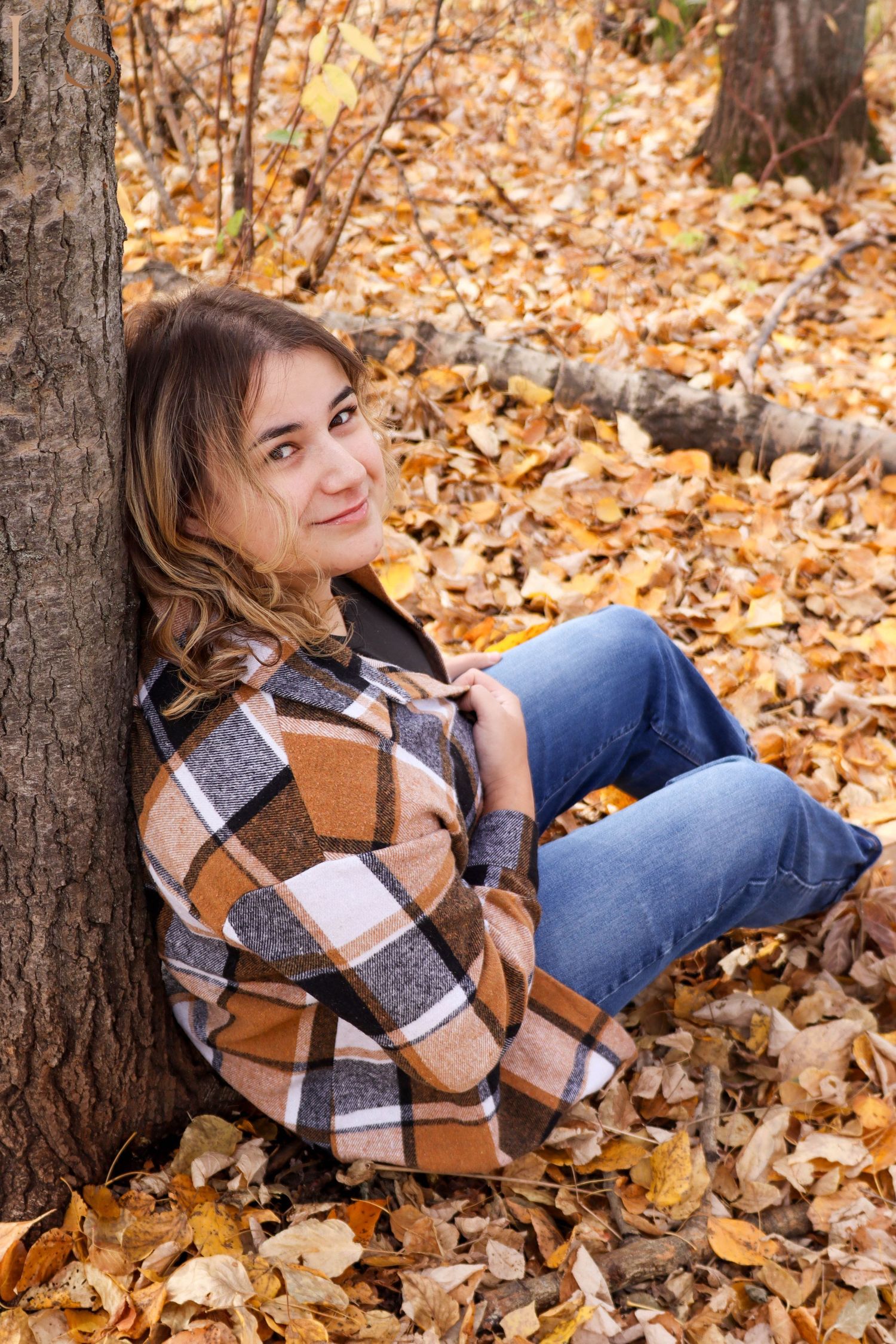 Autumn portrait session with someone lying in fallen leaves wearing a plaid jacket.