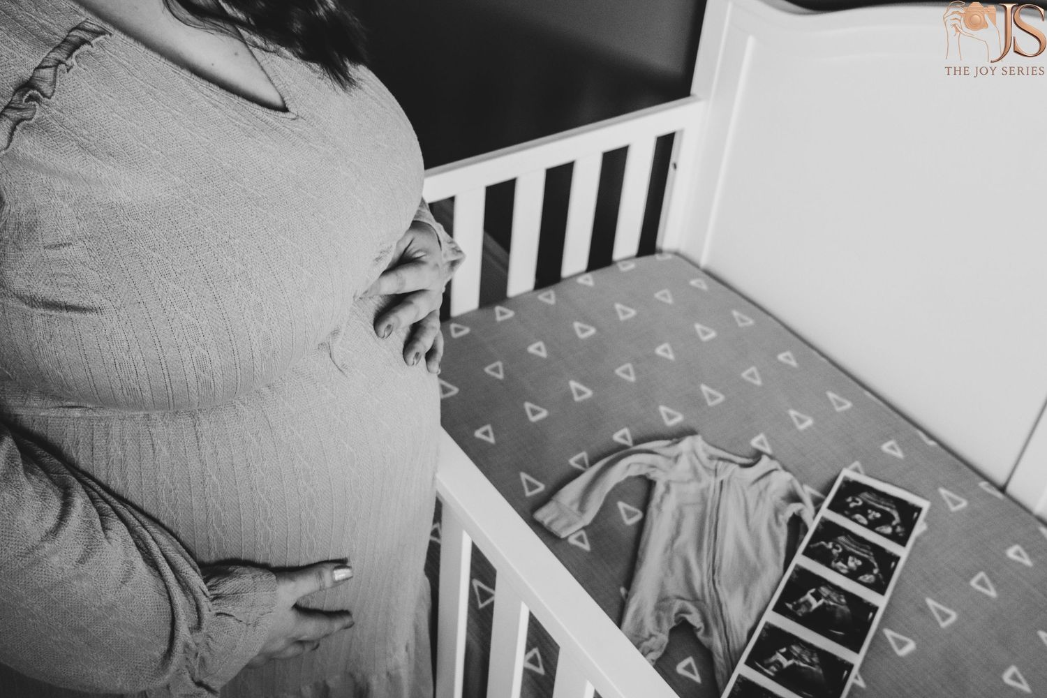 Black and white photo of a decorated nursery crib with alphabet bedding and ultrasound photos displayed.