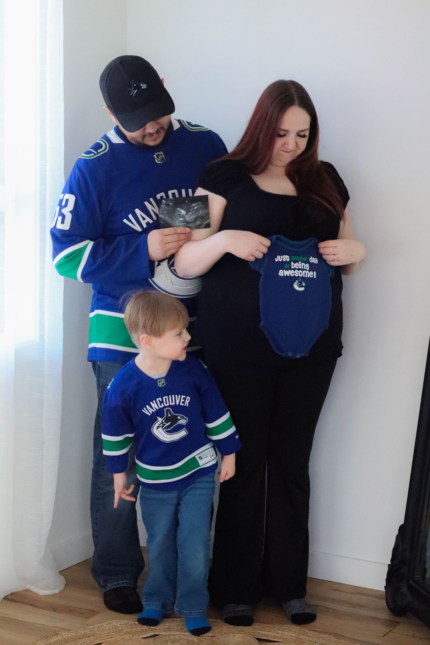 Family wearing matching hockey jerseys while holding baby clothes for pregnancy announcement.