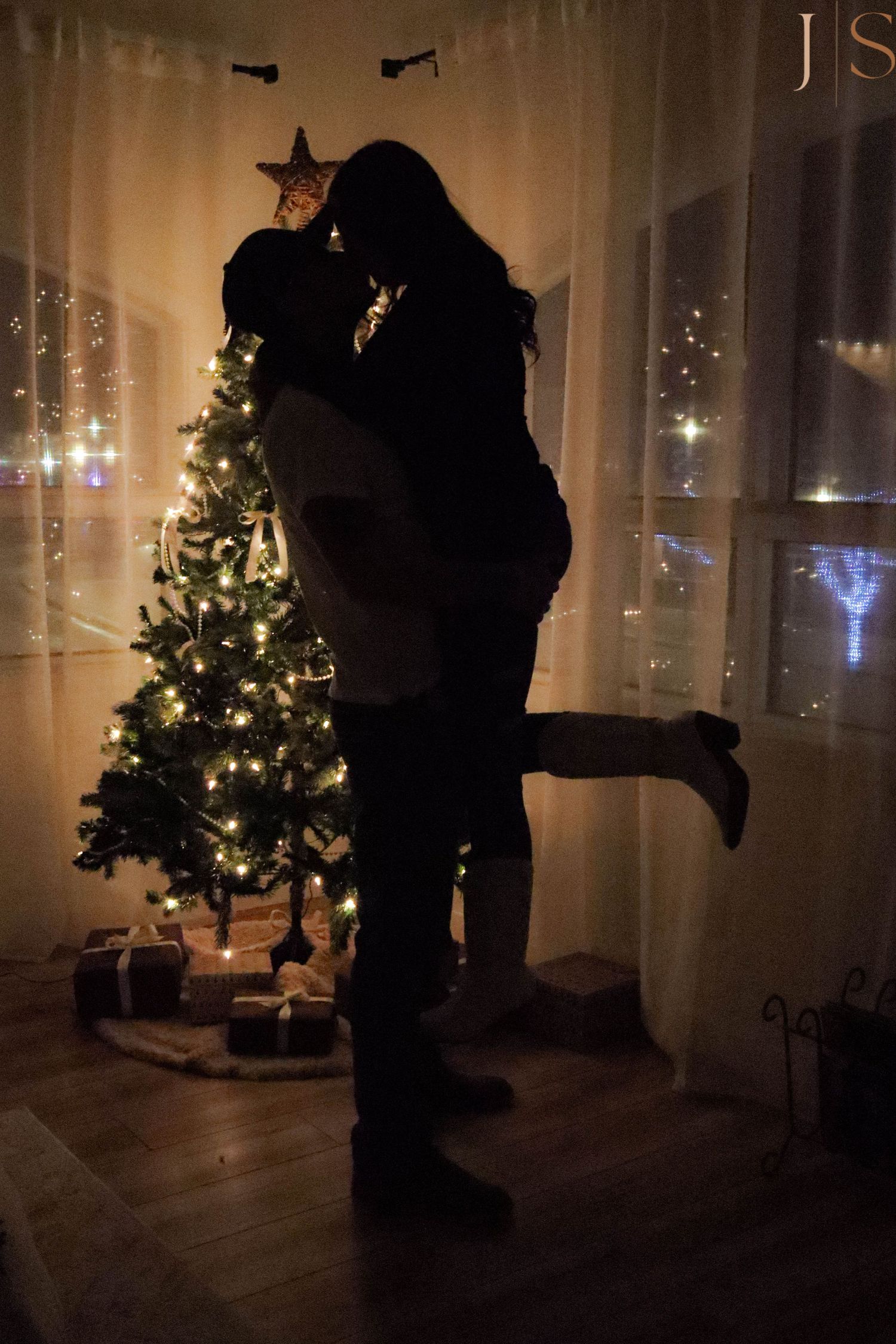 Silhouettes of people dancing in front of a Christmas tree with twinkling lights in a dark room.