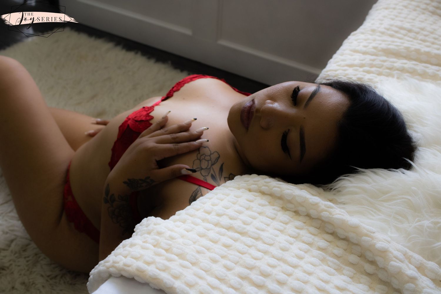 A person in red lingerie laying on white textured bedding in soft lighting.