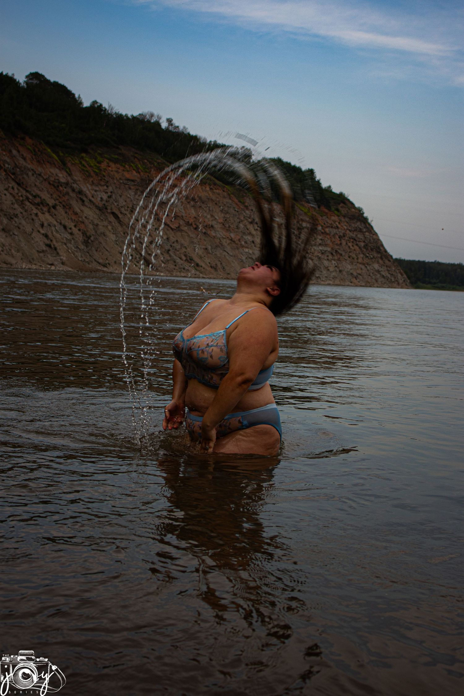 A playful summer scene of someone flipping their hair back in shallow water near a cliff.