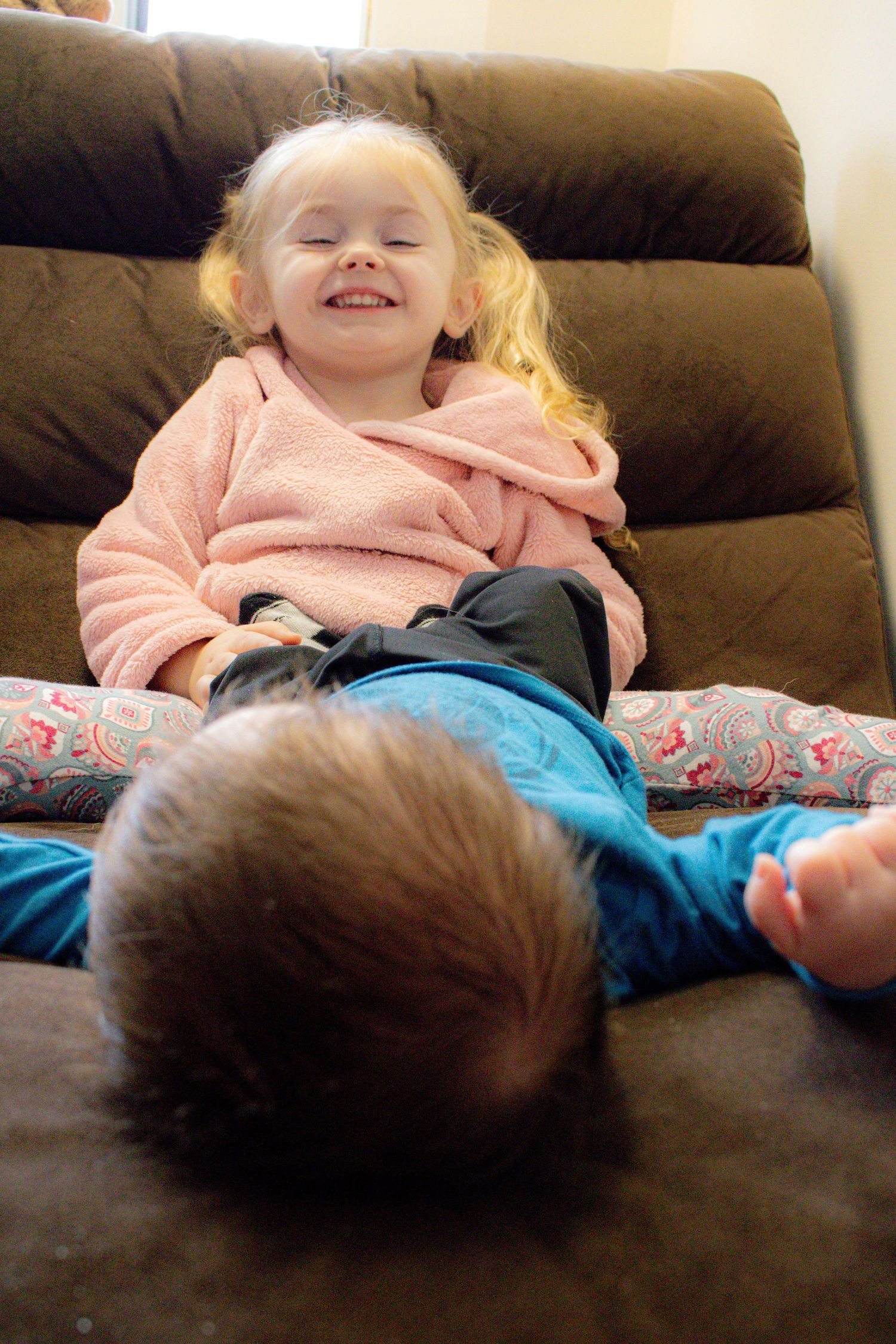 Young child laughing while relaxing on a brown leather couch.