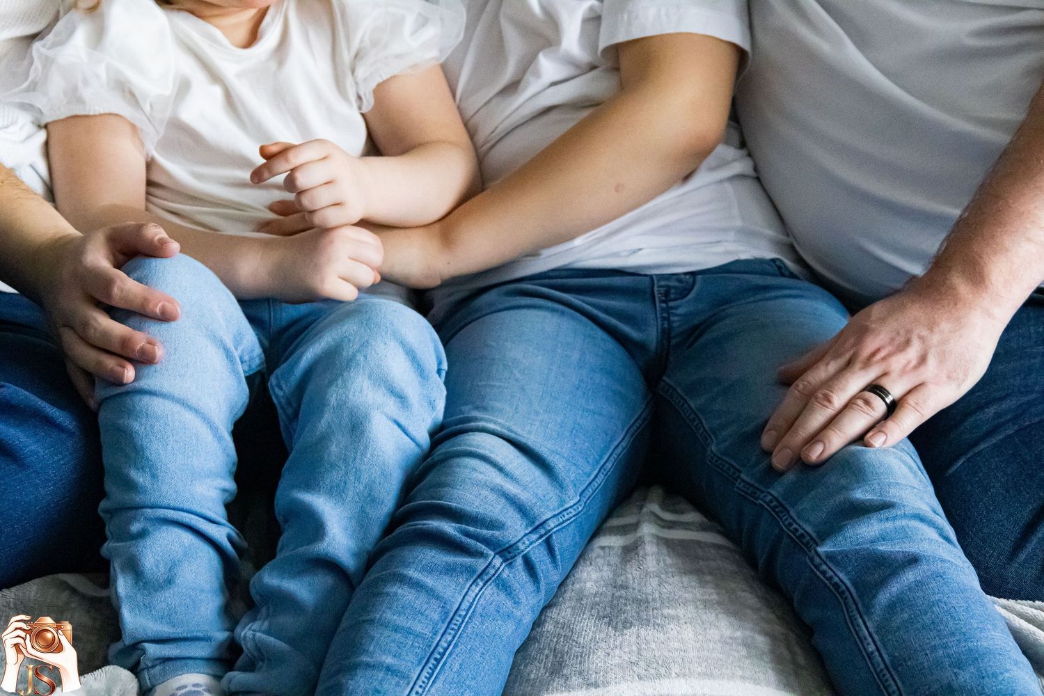 A casual lifestyle photo shows denim-clad legs of people sitting together on a white bed.